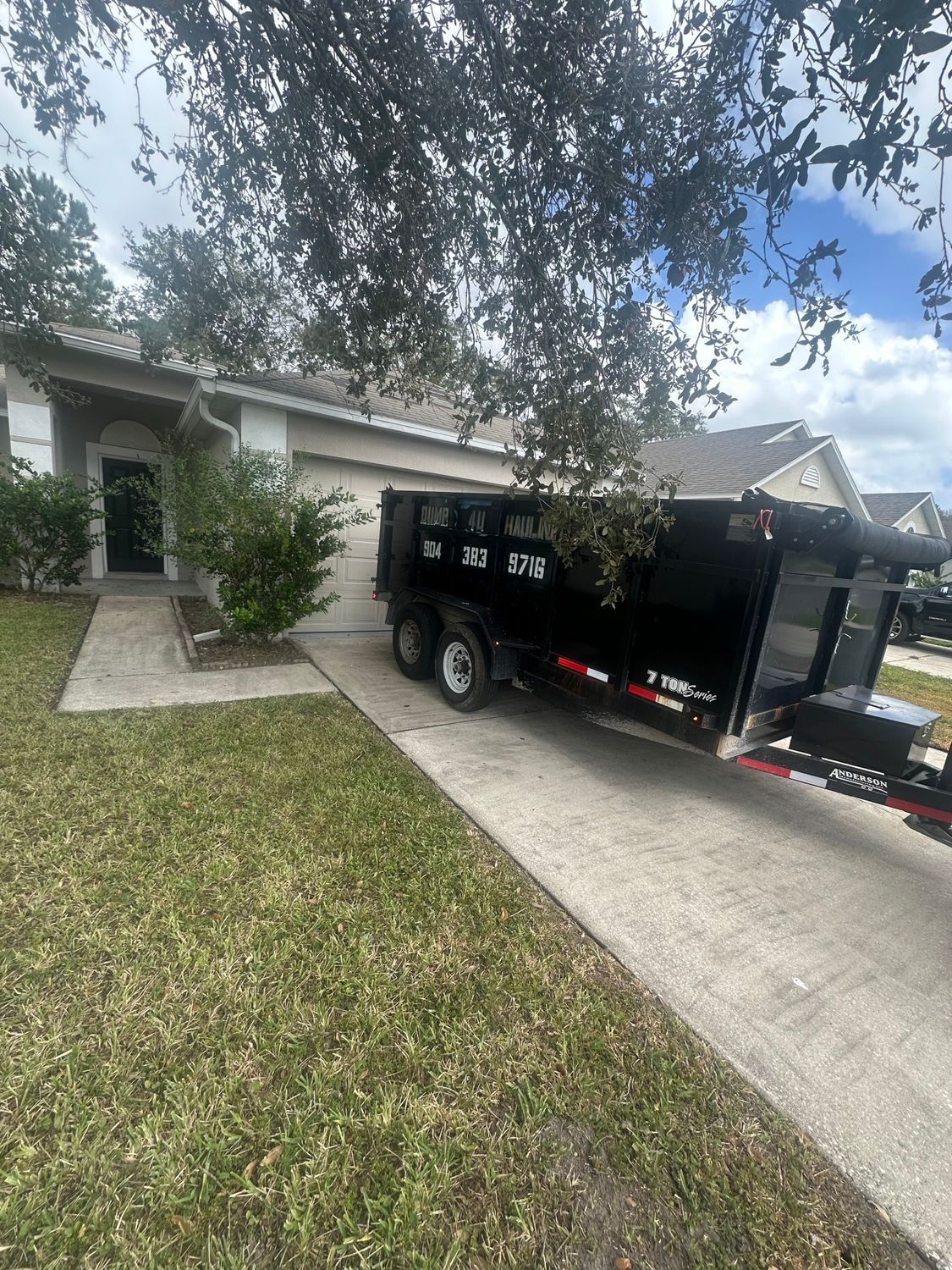 Construction site with a green dumpster in front of a partially built building with exposed wooden framing and siding.