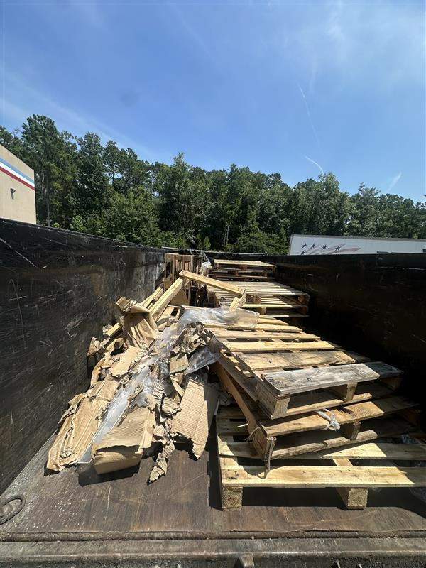Two overflowing green dumpsters outdoors, filled with garbage and cardboard.