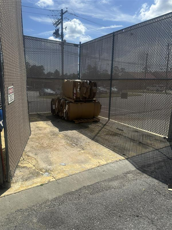 Orange dumpster filled with debris on green grass next to a road, tree, and parked cars.
