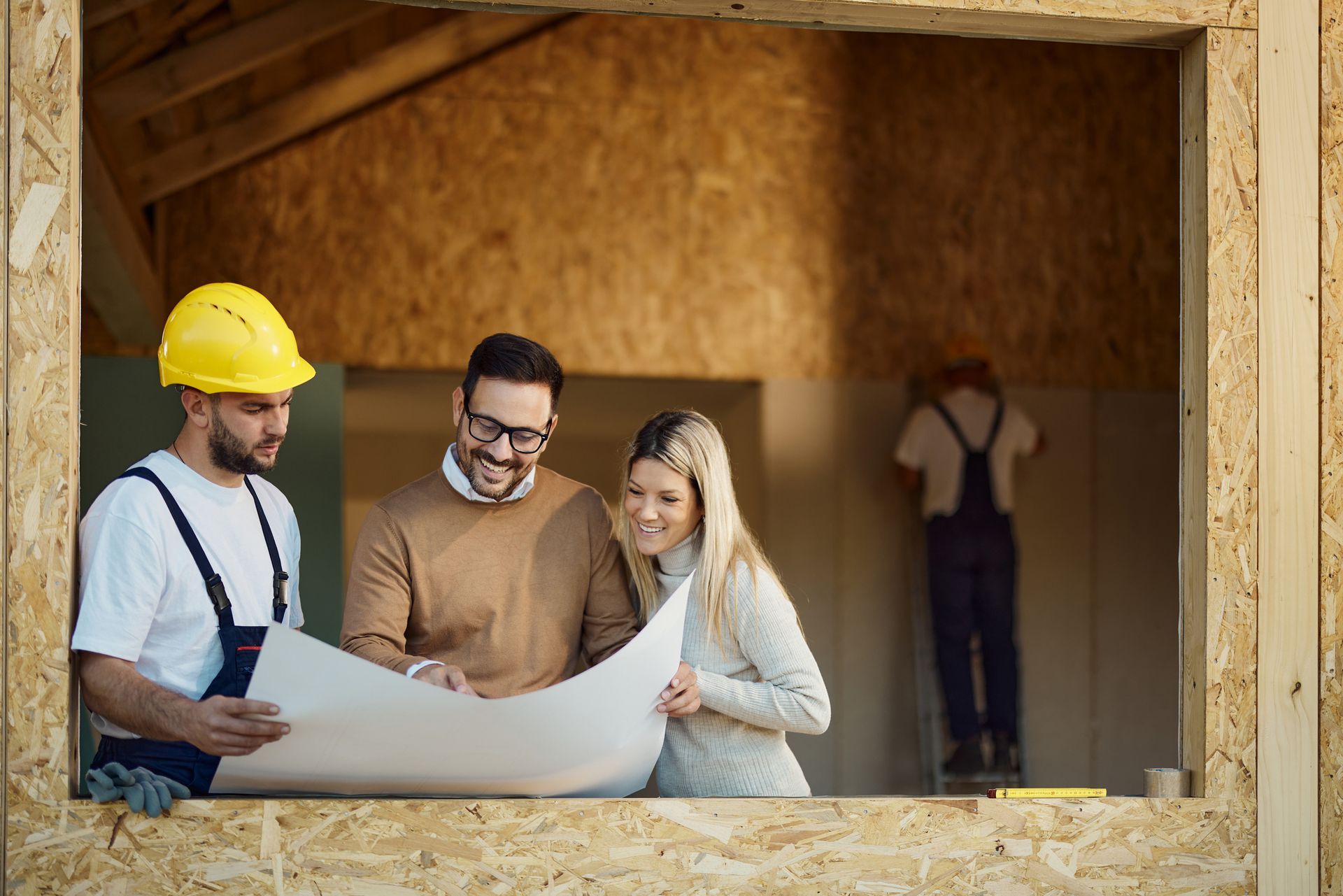 Happy couple analyzing blueprints with manual worker at construction site.