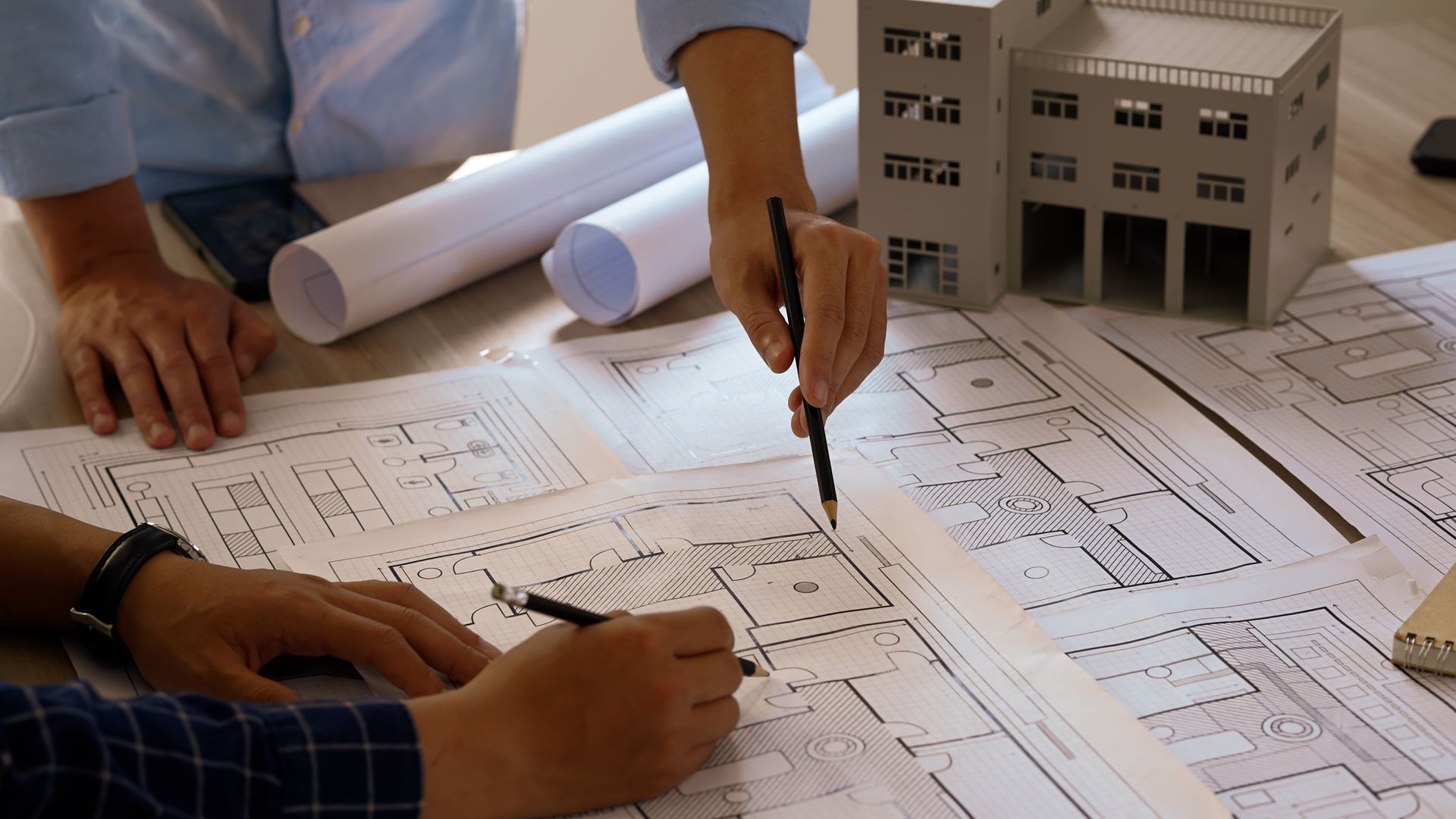 Architects working on blueprints with a model building on the table.