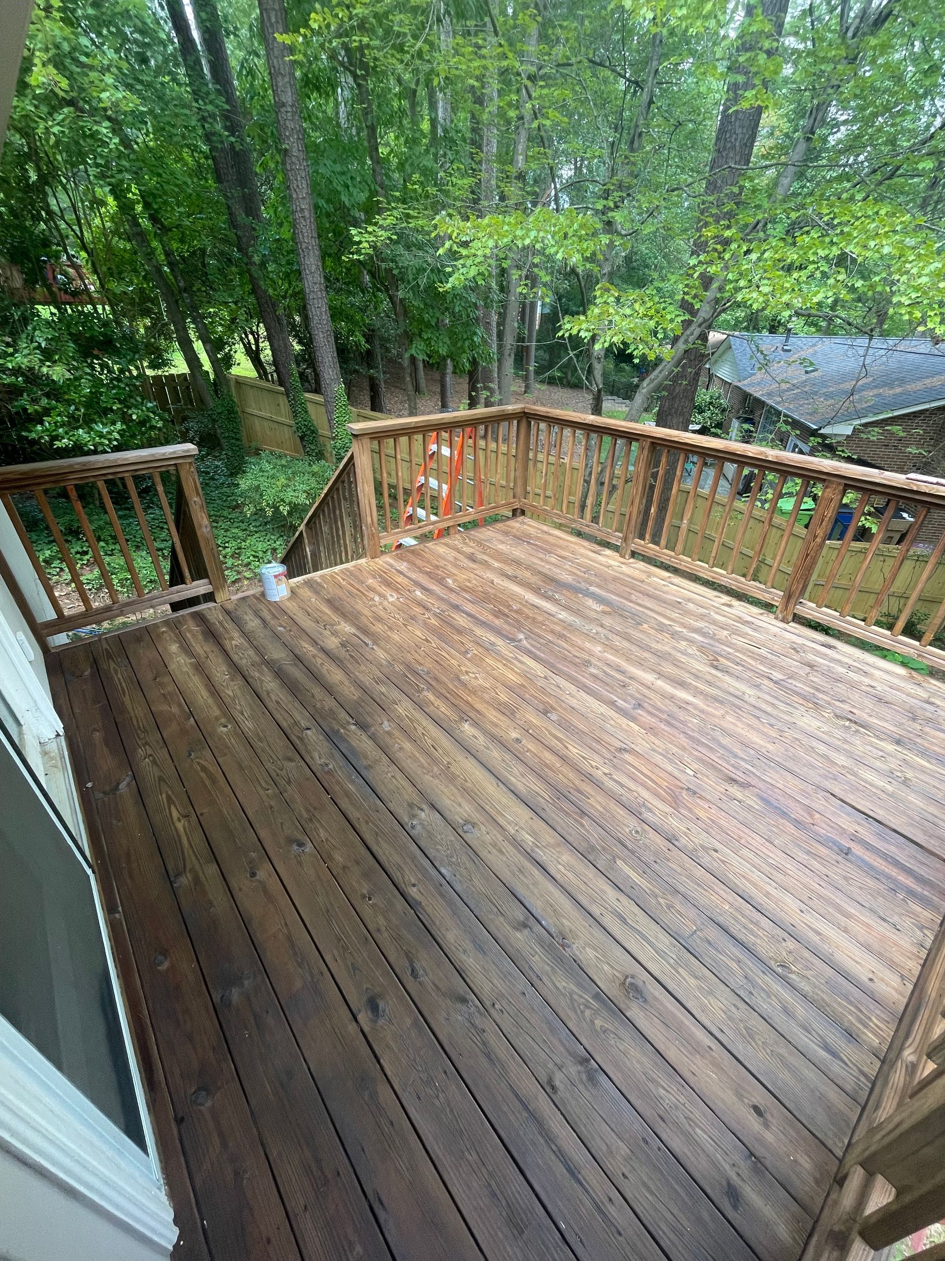 Wooden deck surrounded by railings, overlooking a backyard with trees.