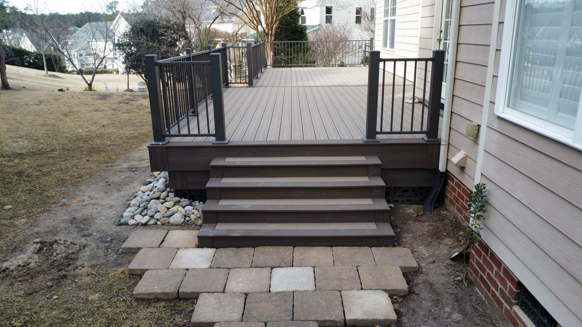 Deck with steps leading to a yard, brown composite material, brick pathway.