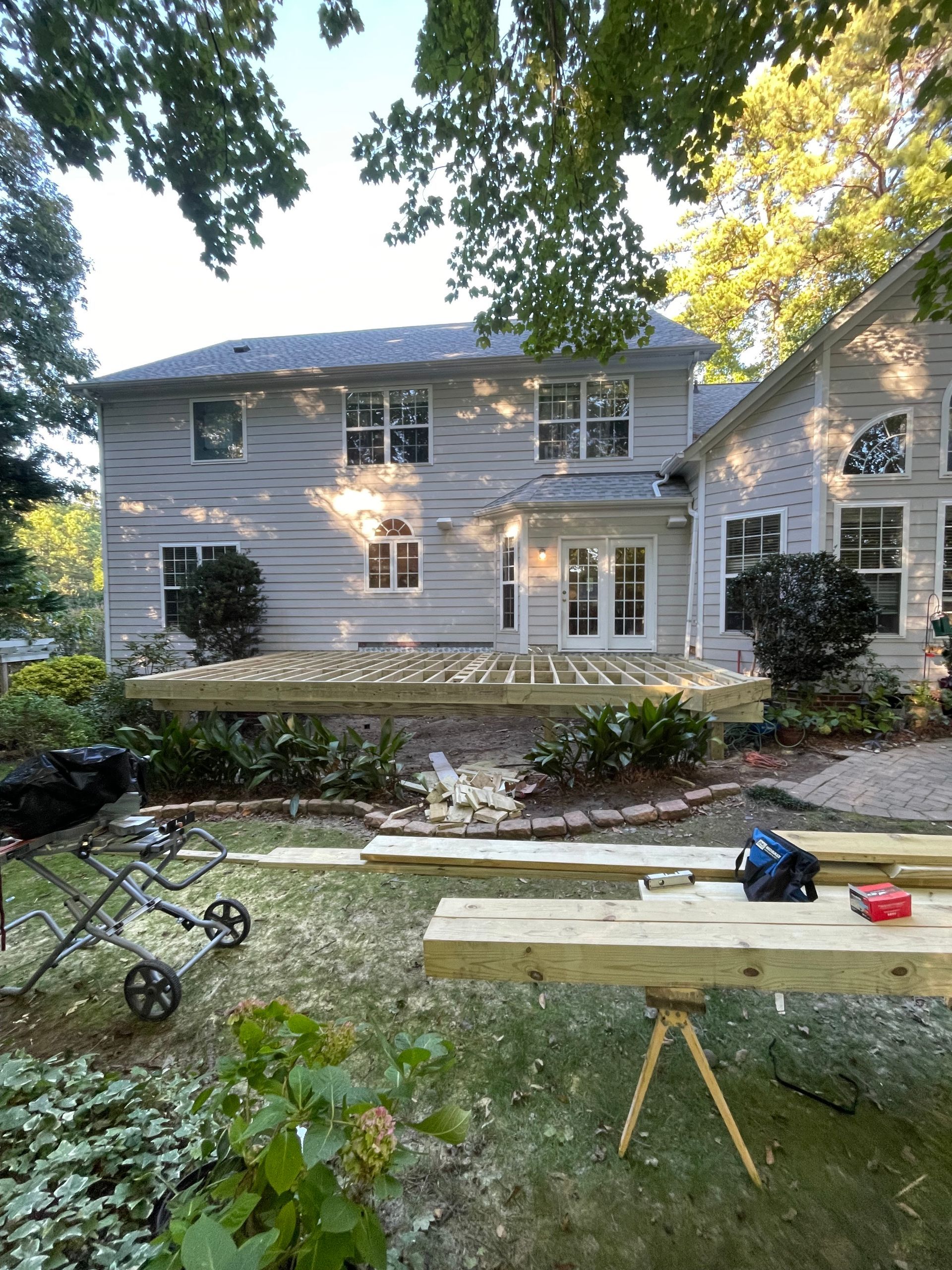 Backyard deck construction in progress; house in the background. Lumber, tools, and partial deck visible.