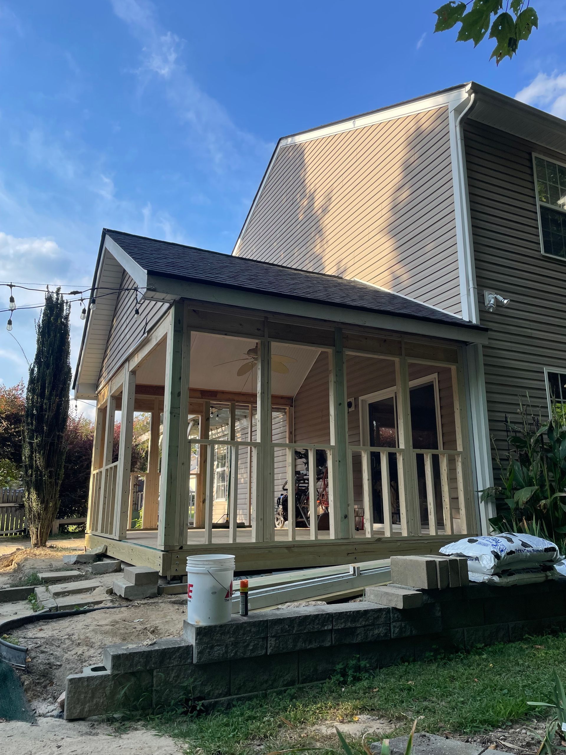 Newly constructed screened-in porch attached to a two-story house, with wooden railing and supports. Blue sky in background.