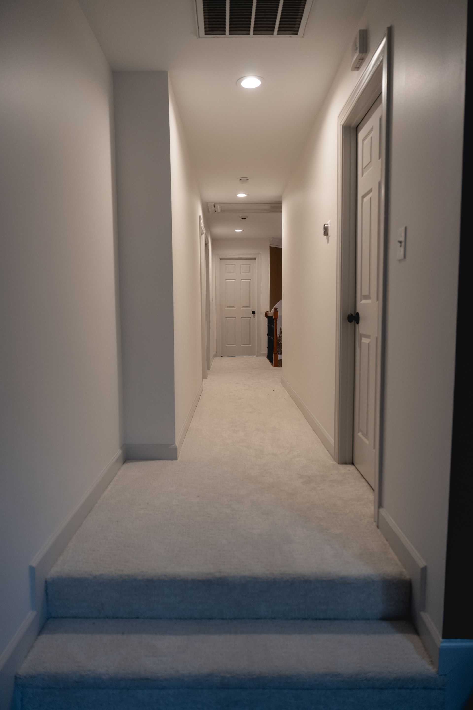 Long hallway with white walls, carpeted floor, and doors.
