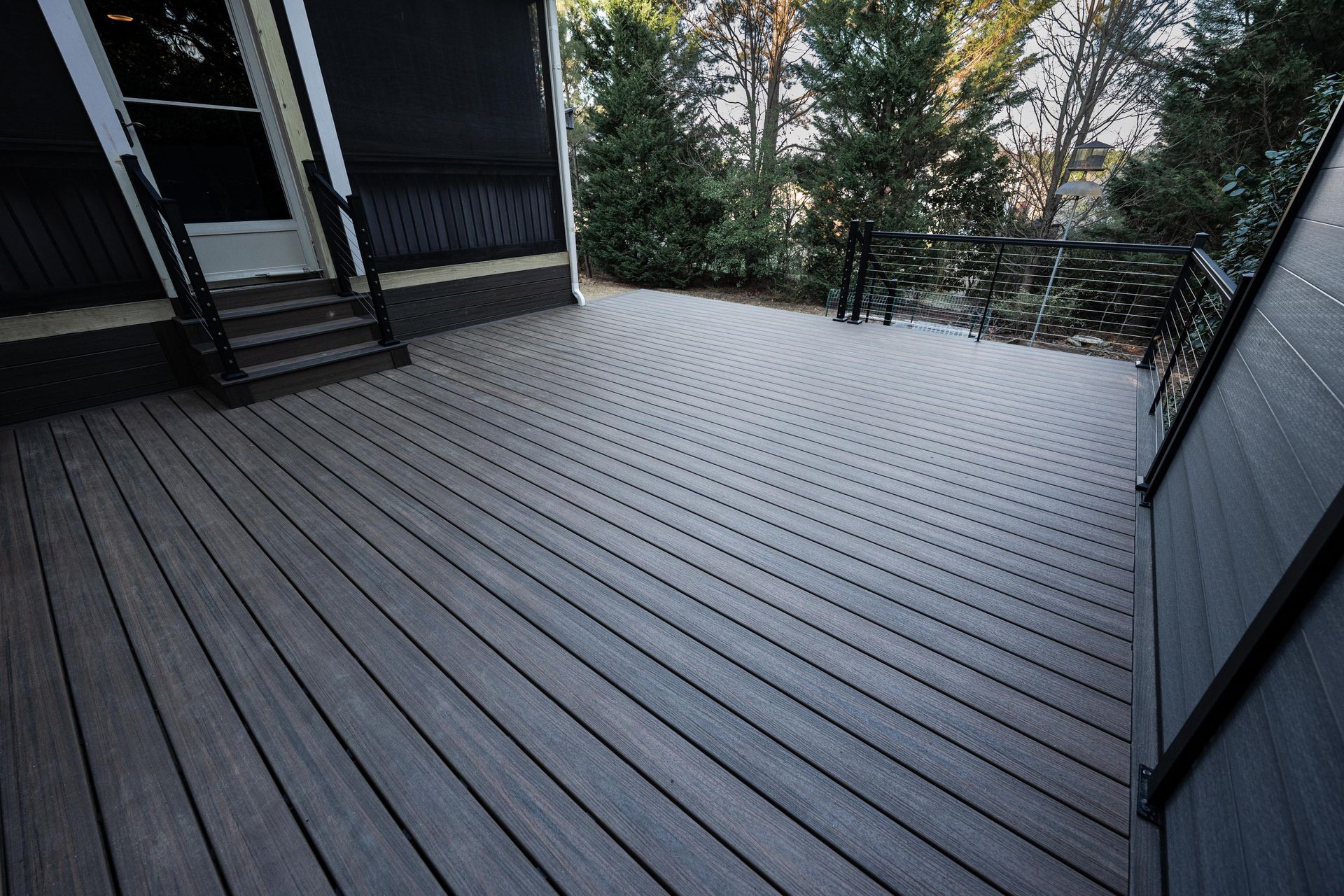 Gray composite deck with a circular pattern design, stairs leading to a house entrance, and black railing.
