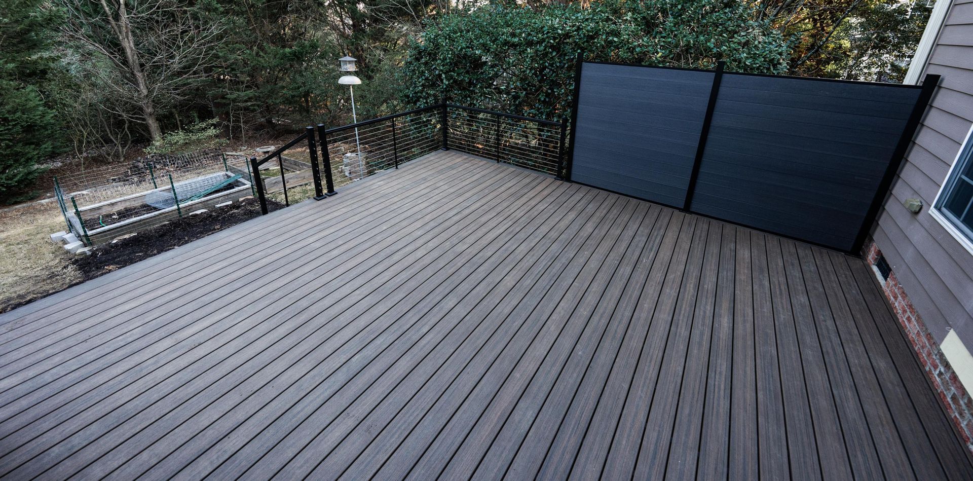 A wide, dark brown wooden deck features a black privacy screen along a siding wall and a black metal railing.