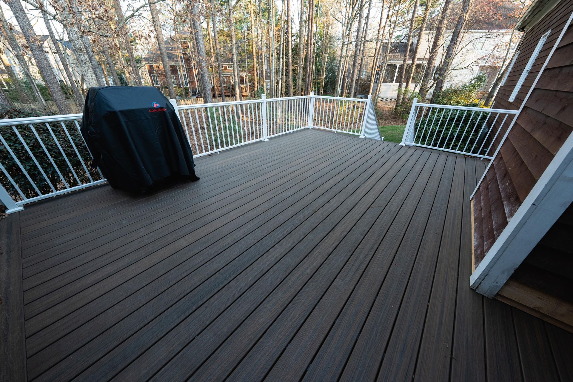 A dark brown composite deck with white railings and a grill covered by a black tarp, viewed from a slightly elevated angle.