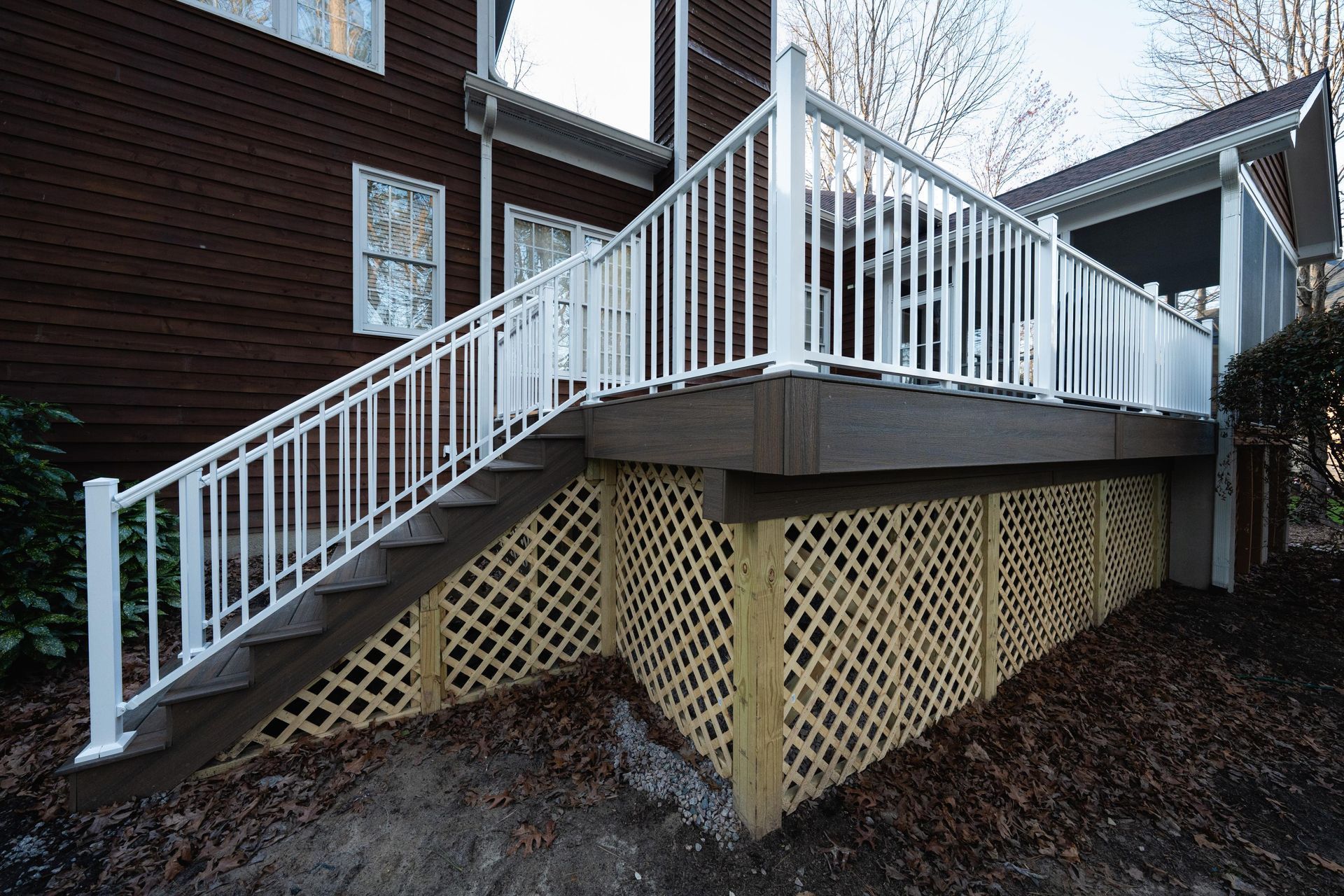 A dark brown wooden deck with white railings and stairs, featuring decorative lattice skirting along the base.