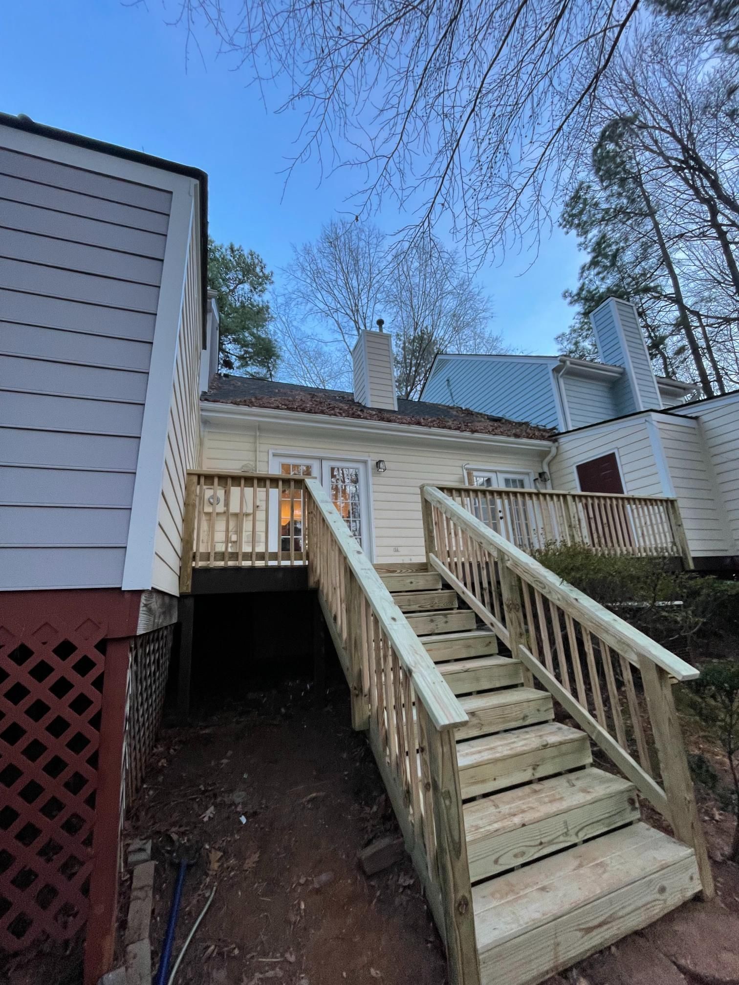 Exterior view of a cream-colored house with a newly constructed wooden deck and stairs leading to double glass doors.