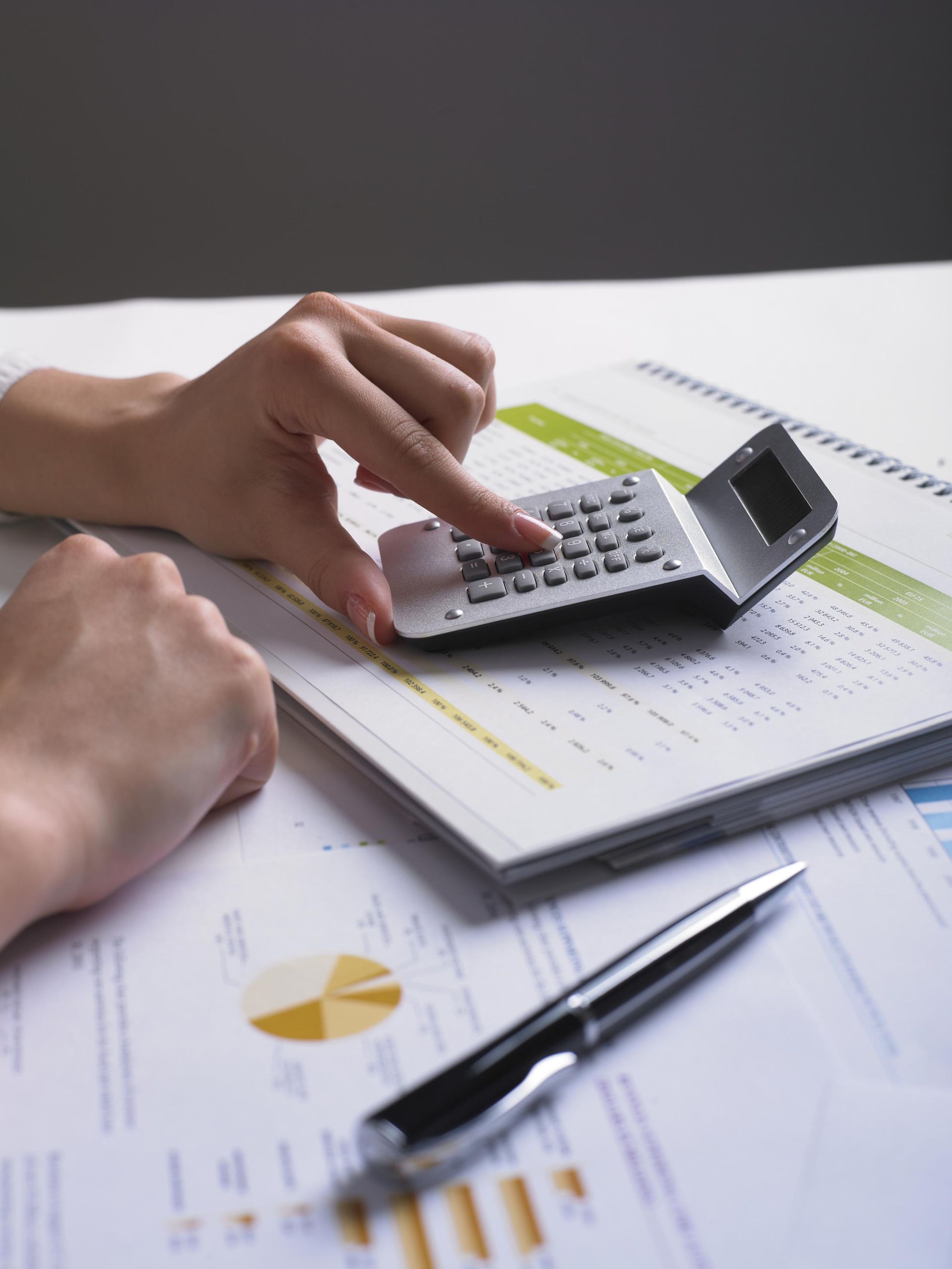Hands using a calculator on top of financial documents with a pen.