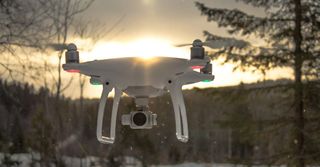 A drone is flying over a snowy forest at sunset.