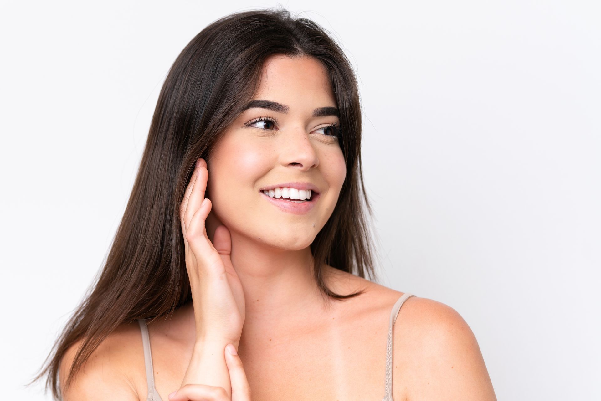 A woman is smiling and touching her face with her hand.