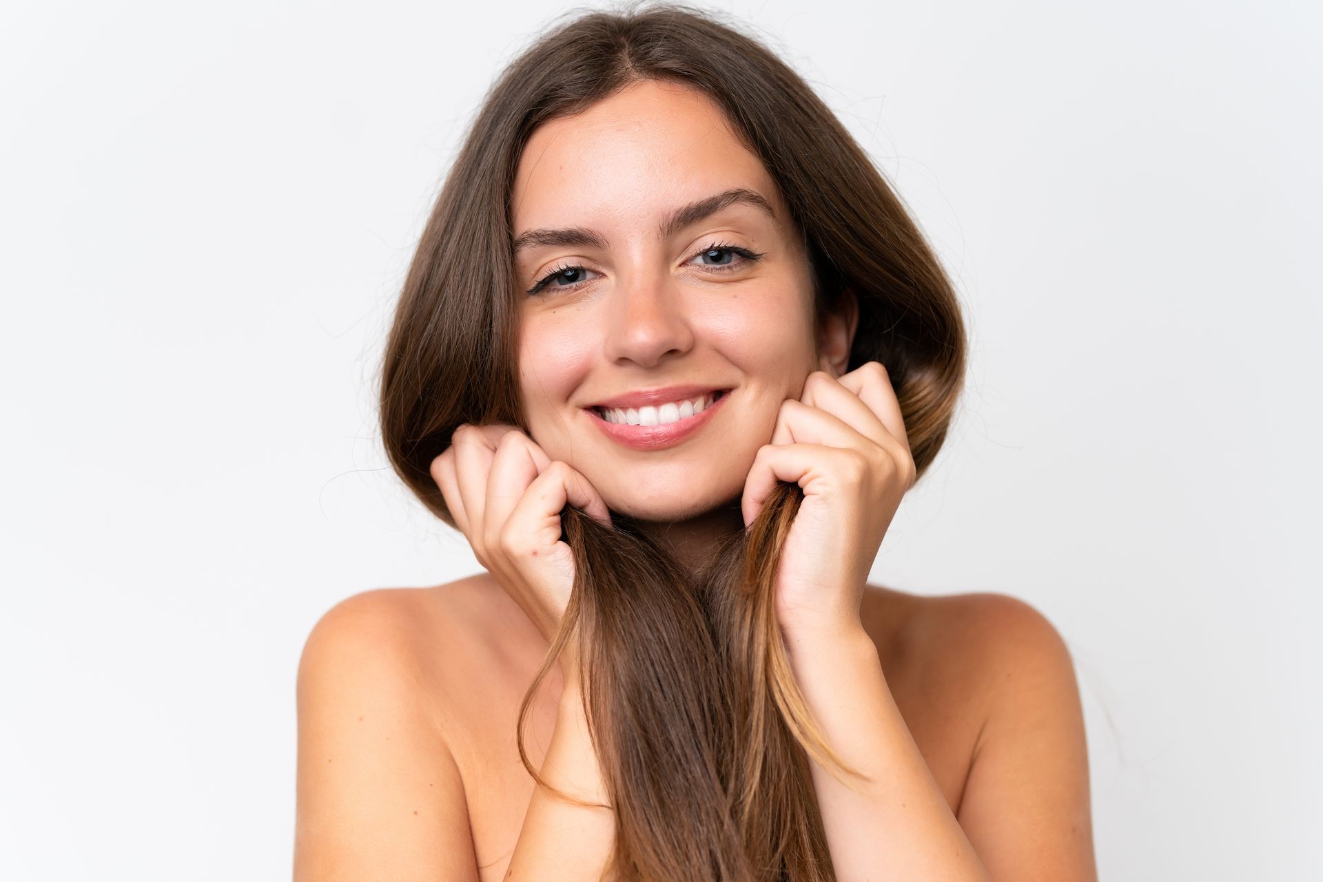 A woman is smiling and holding her hair in front of her face.