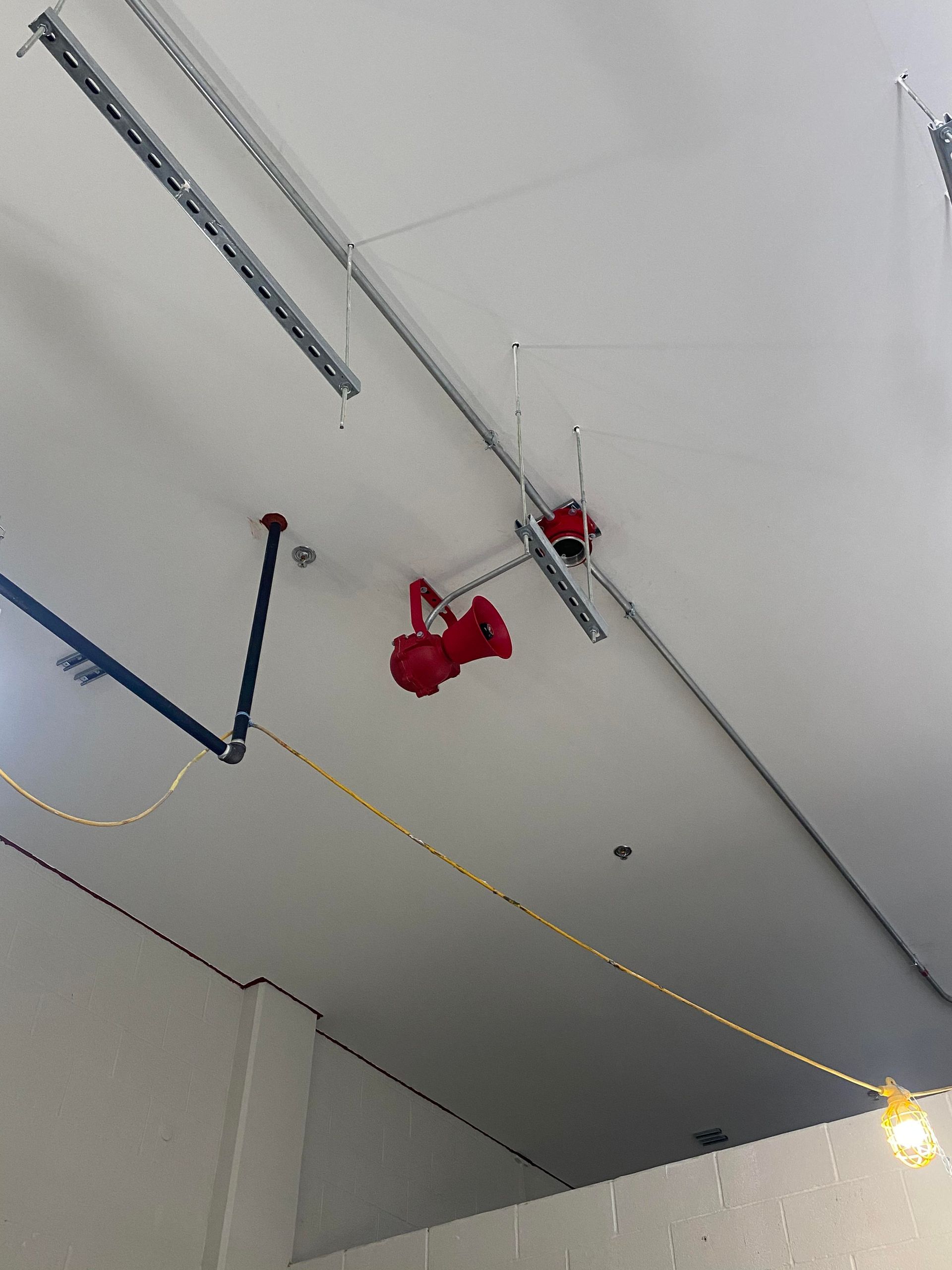 Ceiling with fire sprinklers and pipes; red sprinkler heads, grey ceiling tracks, white ceiling.