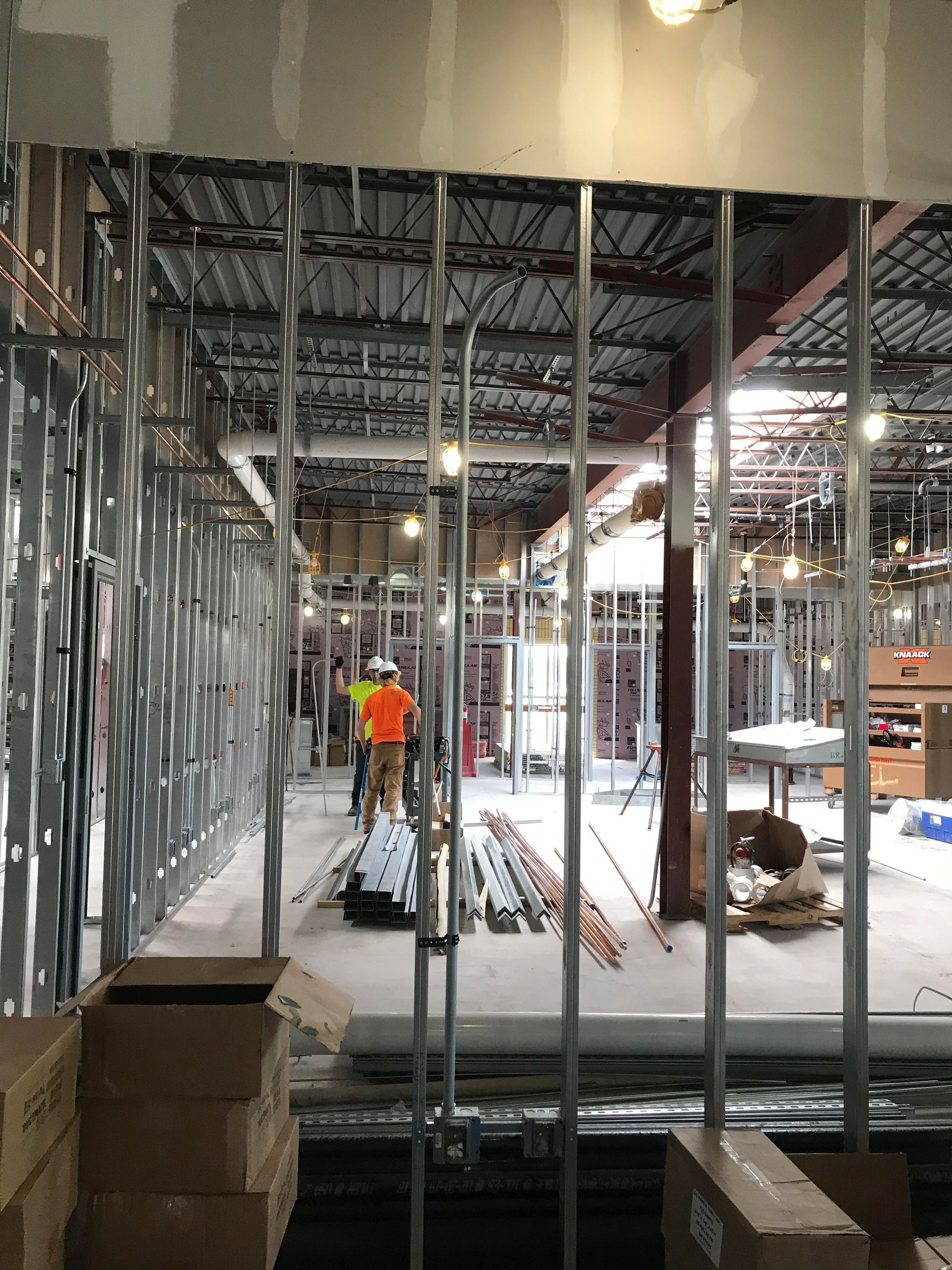Interior construction site with metal studs forming walls; workers in background.