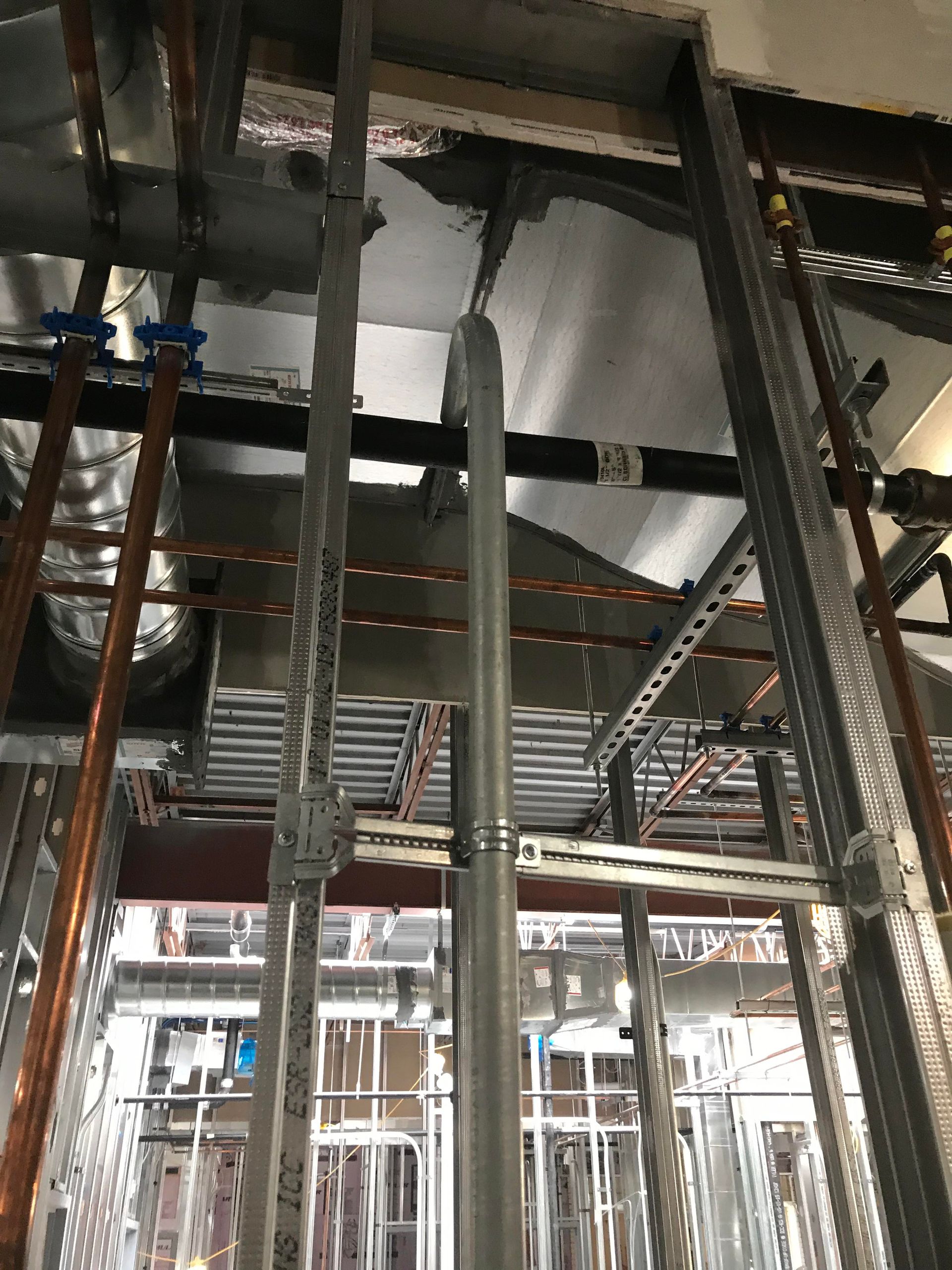 Construction site interior with pipes and electrical conduits running along a ceiling.