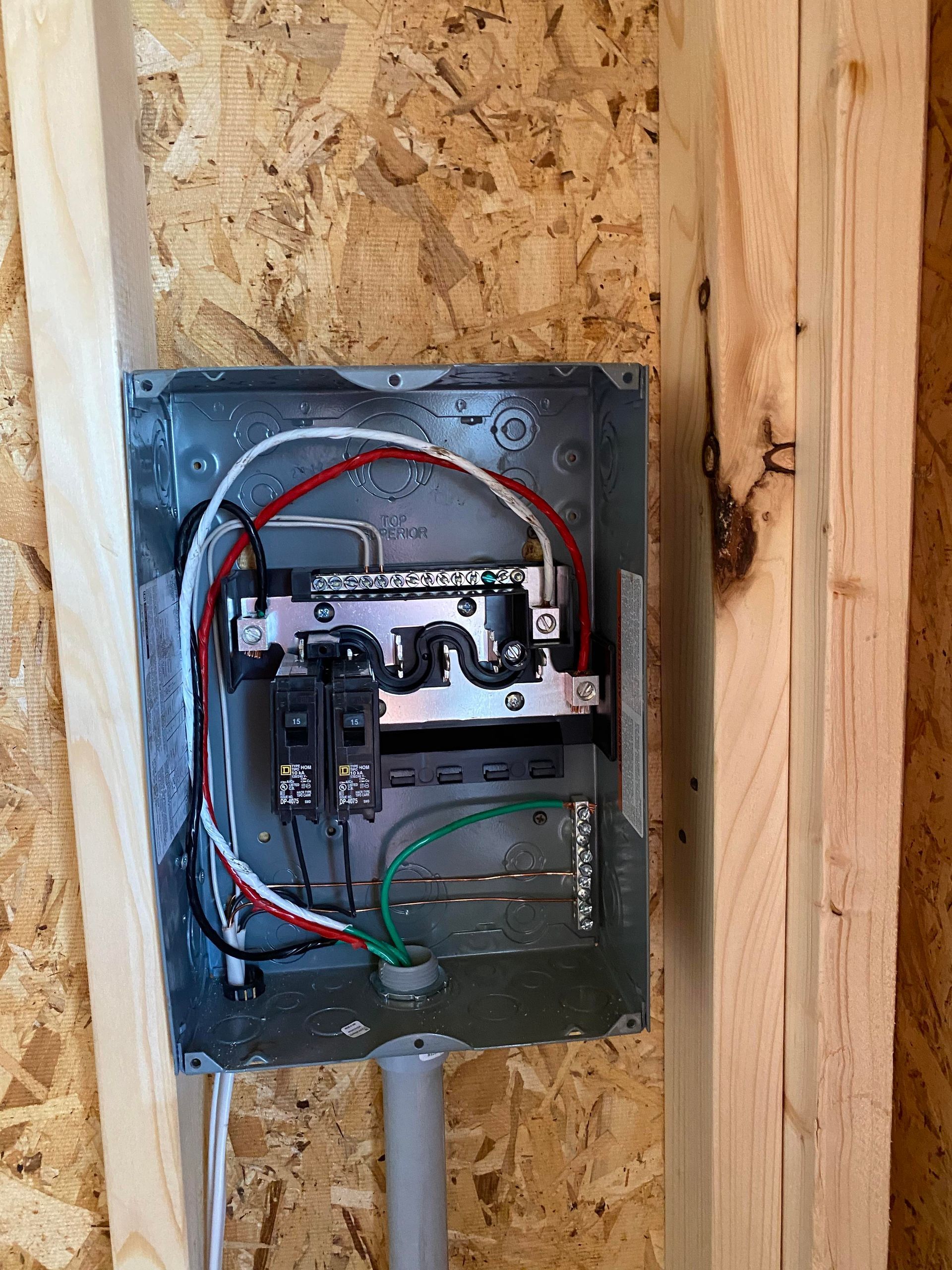 Electrical panel with wires and circuit breakers mounted on wooden framing.