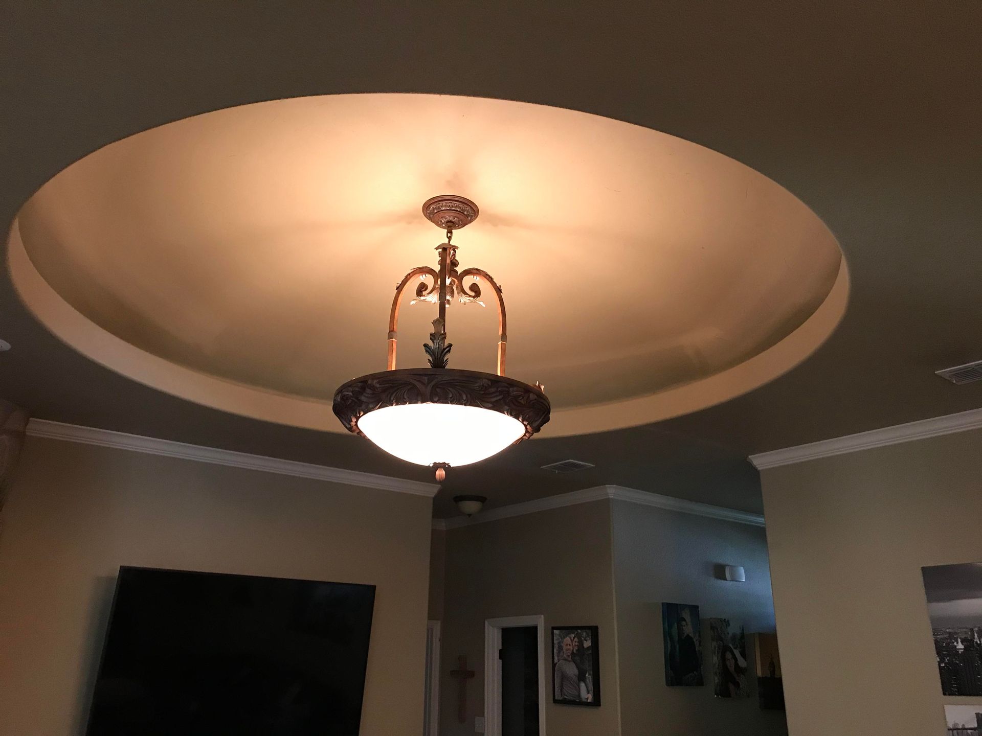 Ornate light fixture hanging from a circular recessed ceiling with ambient lighting.