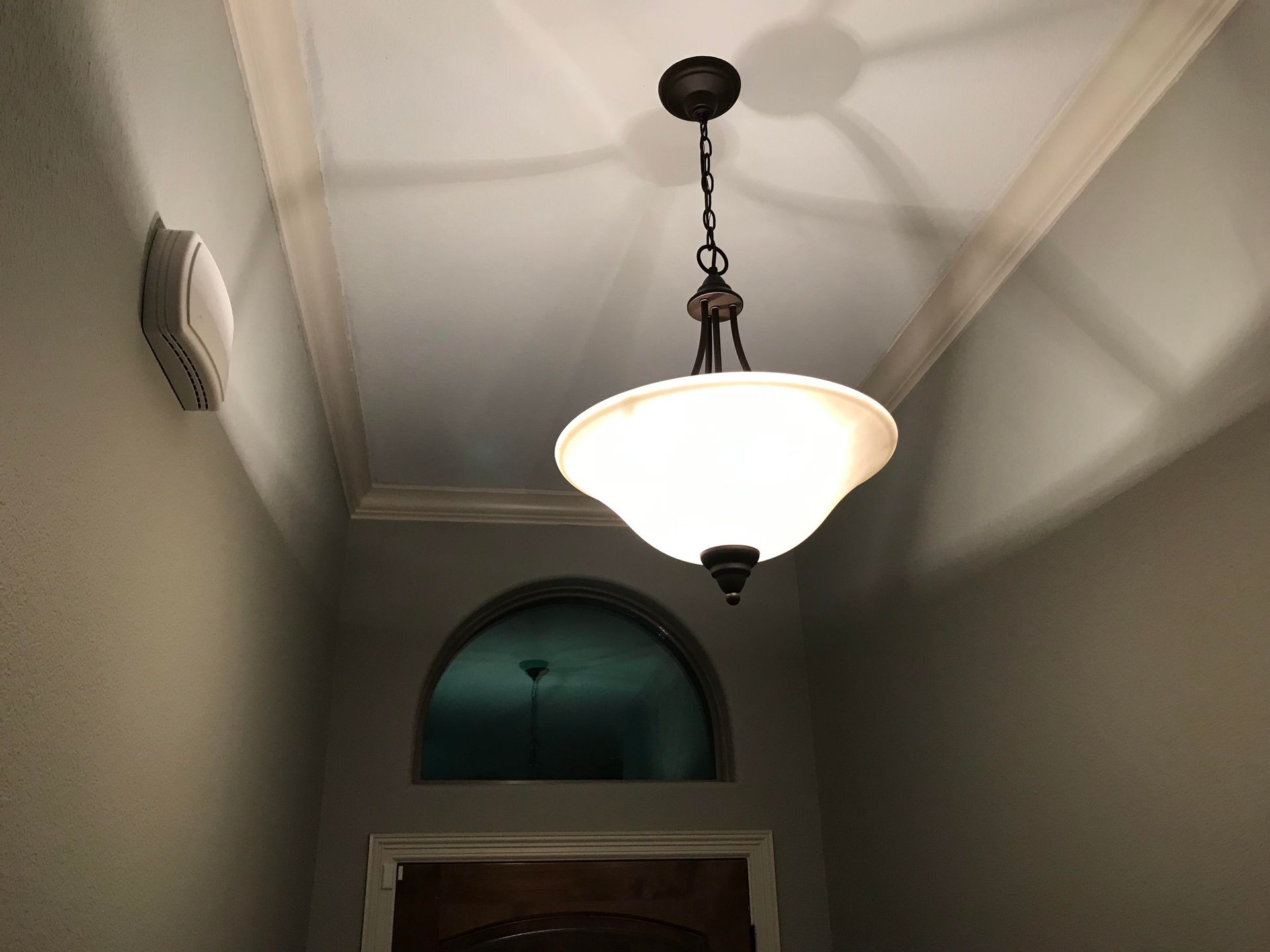 A ceiling light fixture with a frosted glass shade hangs in a room with a white ceiling and gray walls.