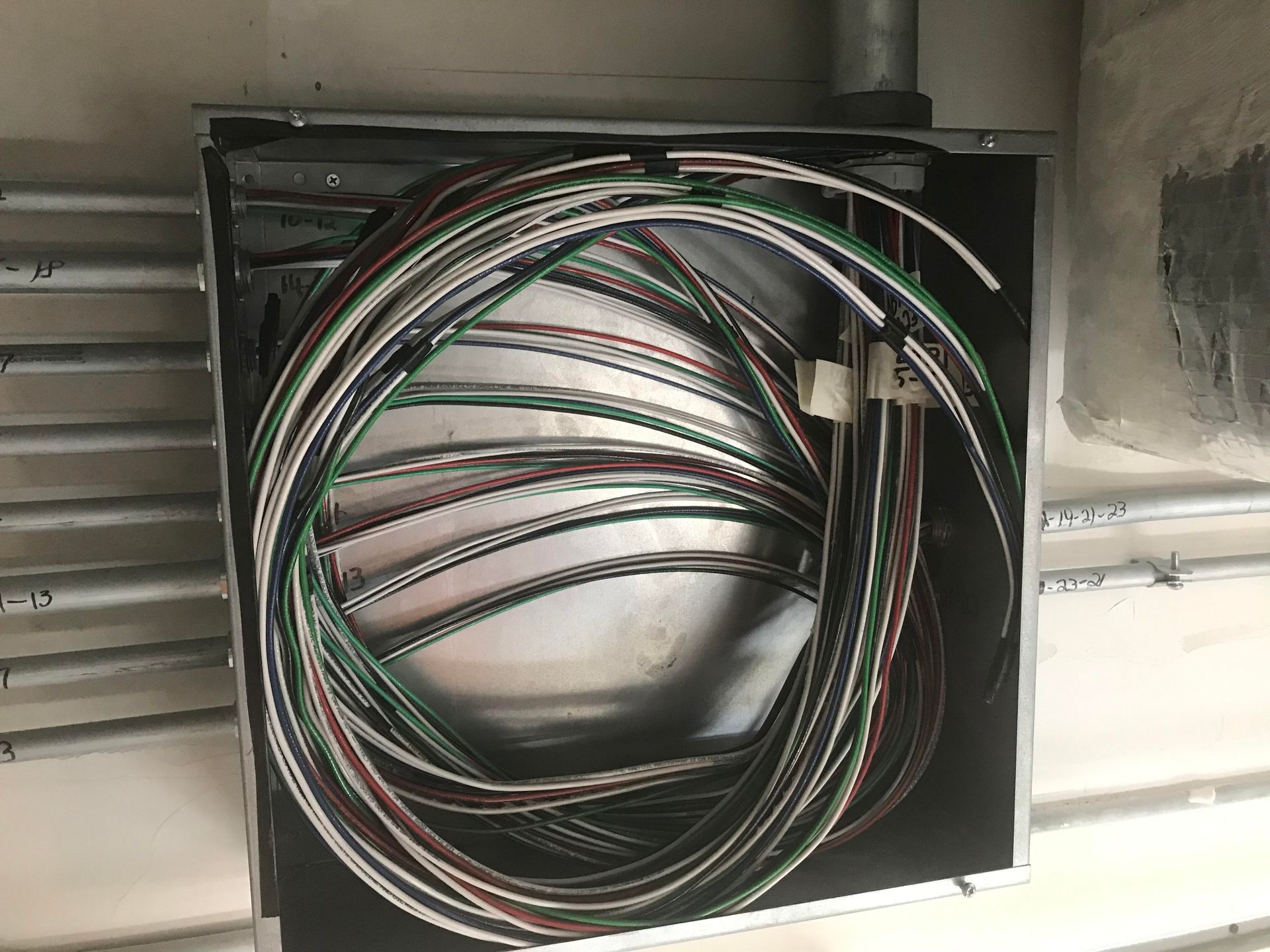Bundle of electrical wires coiled inside a metal junction box on a wall.