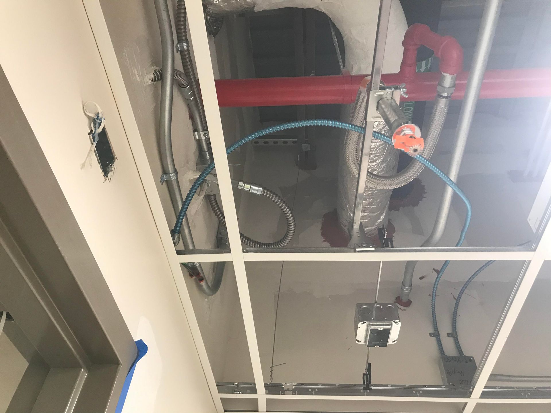 Ceiling with exposed pipes, wiring, and metal grid framework. Blue, red, and silver components.