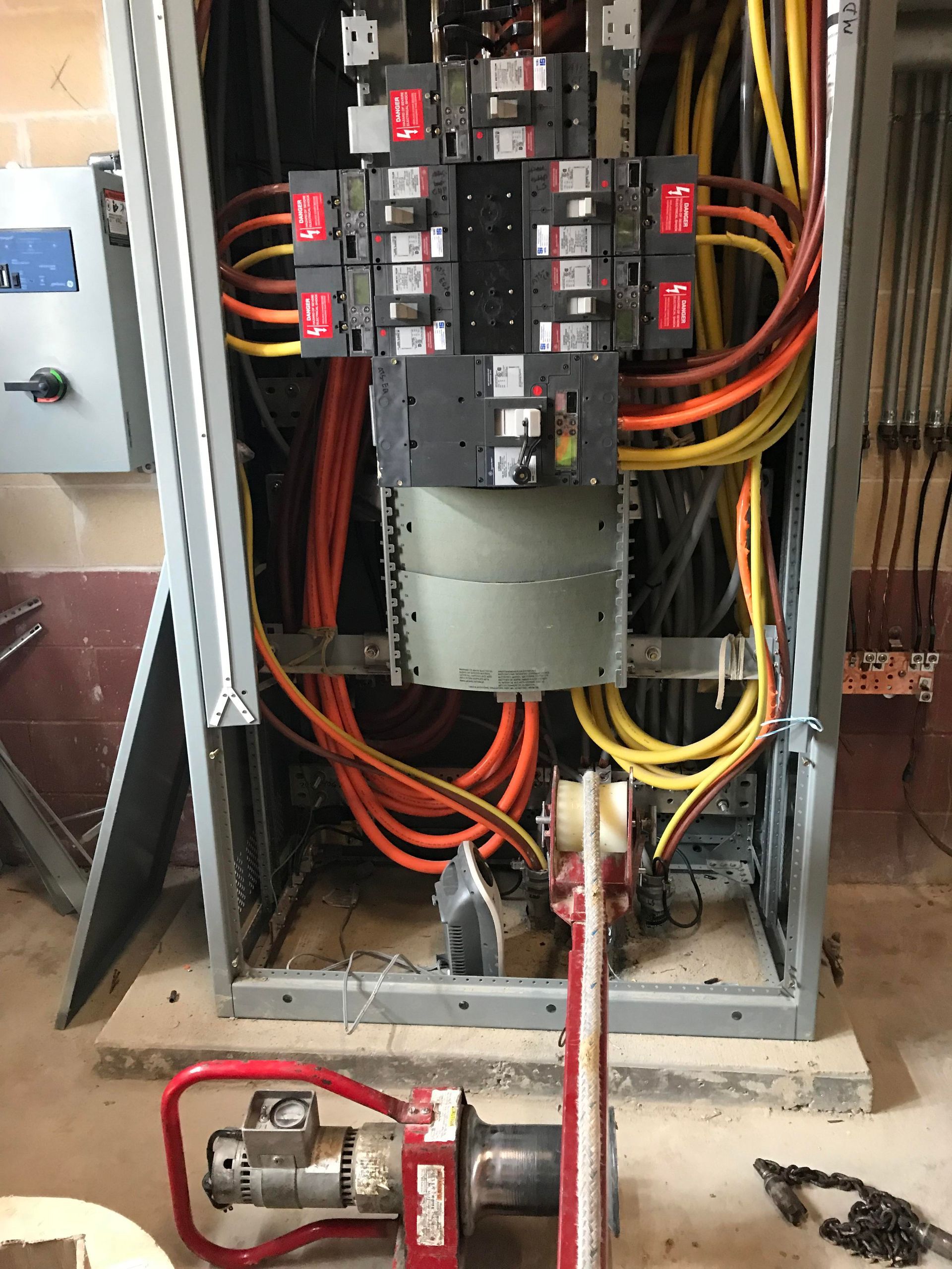Electrical panel with colorful wires and red and black breakers. A tool sits at the bottom.