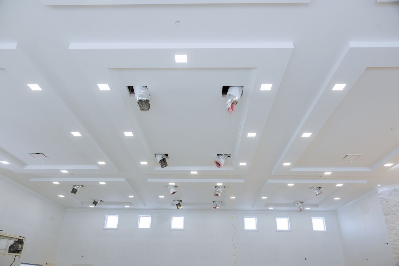 White ceiling with recessed lighting and mounted fixtures in a large room, construction in progress.