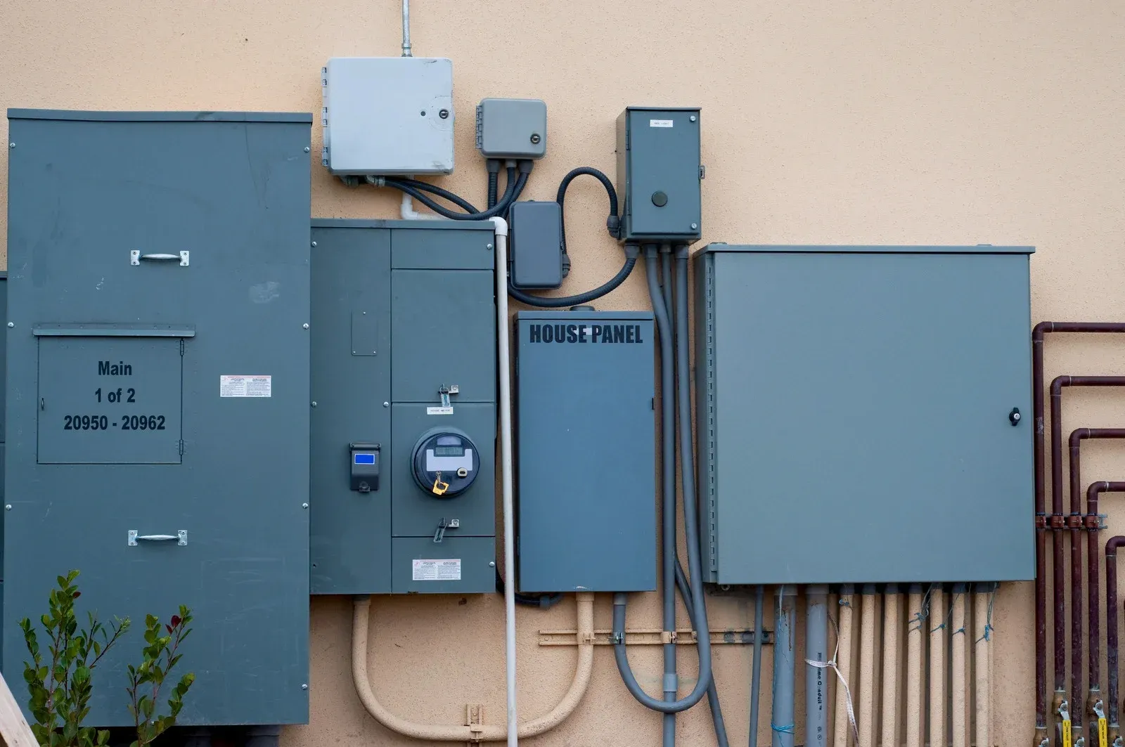 Exterior electrical boxes of various sizes and shapes mounted on a light-colored wall.
