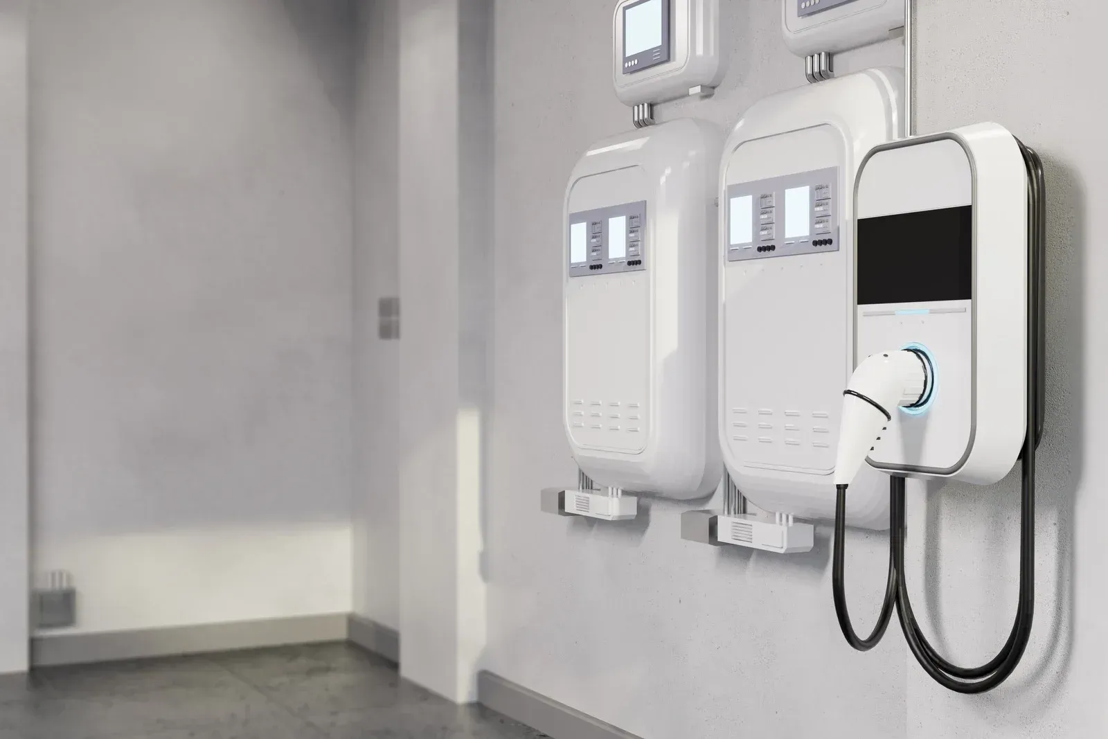 EV charging stations mounted on a wall. White units with displays, one with a charging cable plugged in.