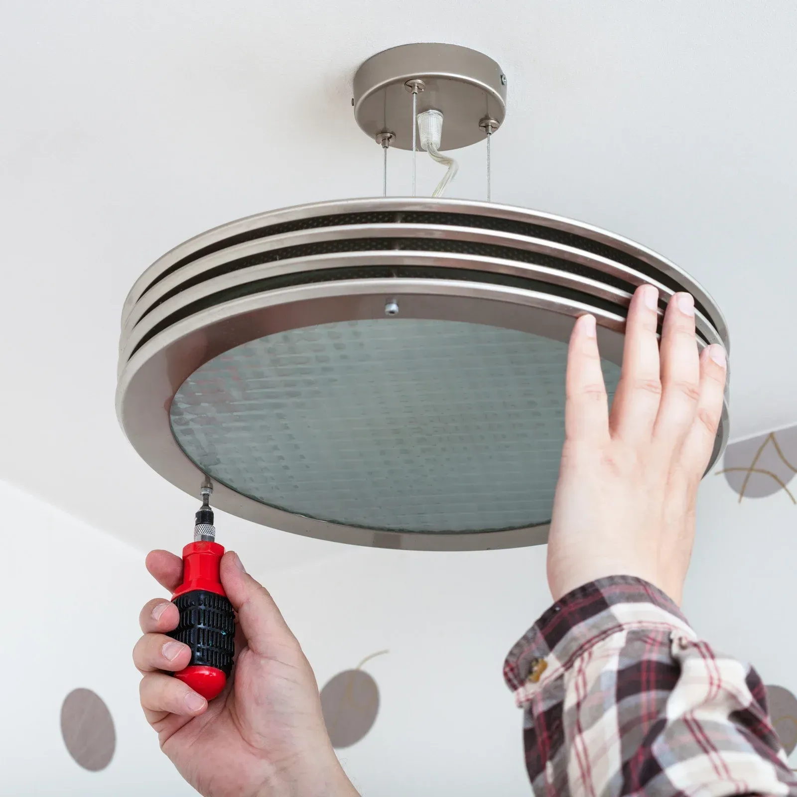 Person using a screwdriver to install or repair a ceiling light fixture.