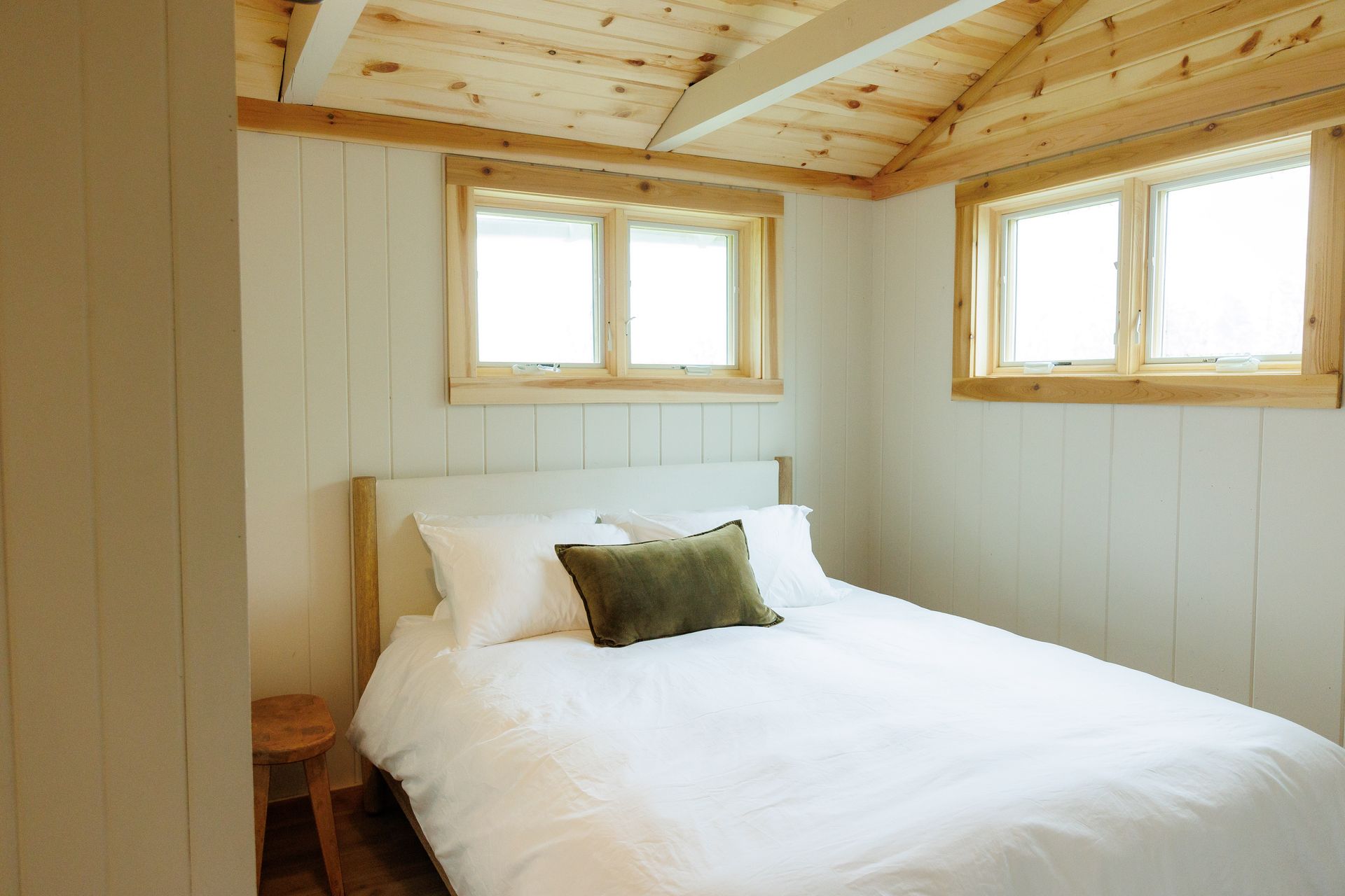 A bedroom with a bed , two windows and a wooden ceiling.