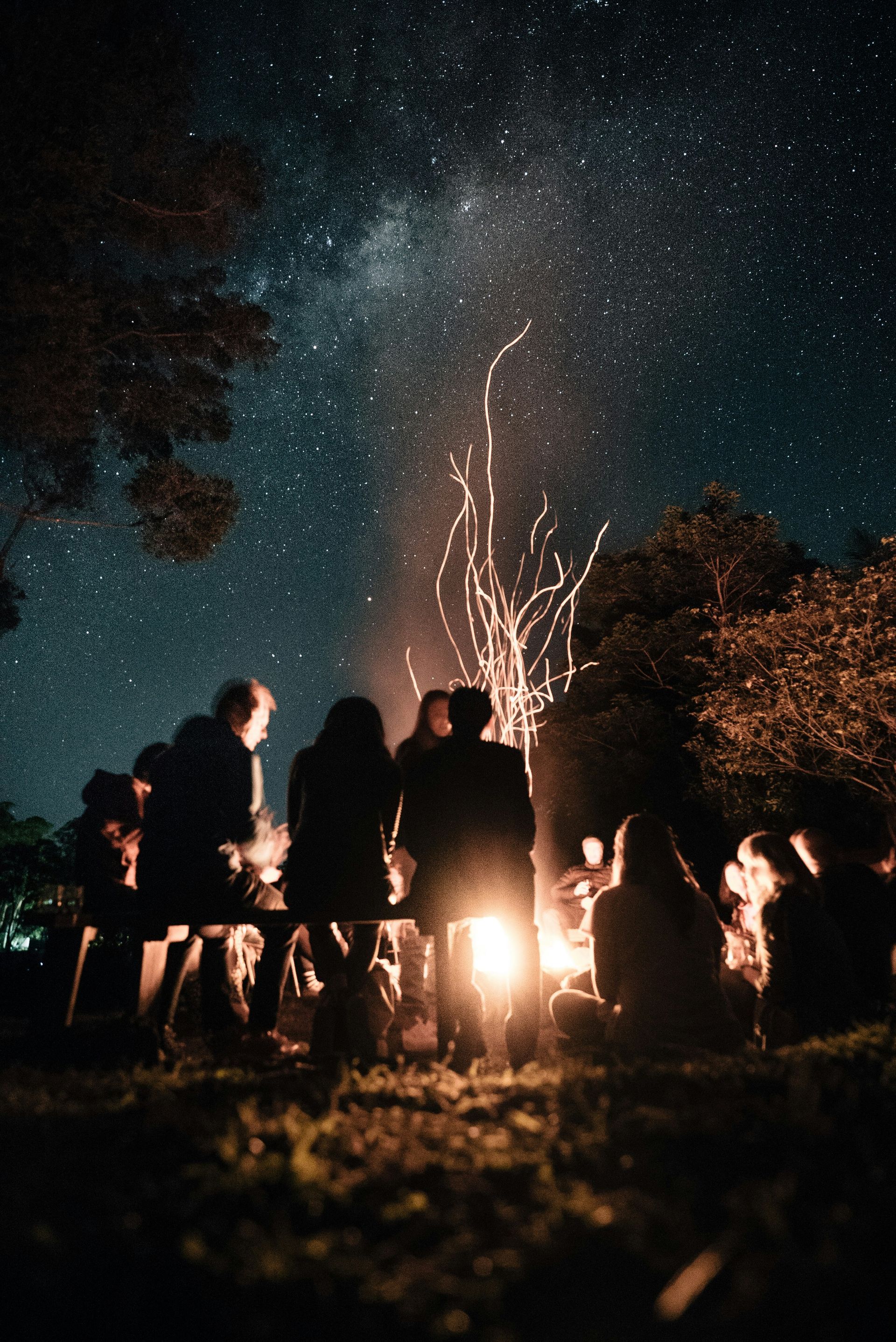 A group of people are sitting around a campfire at night.