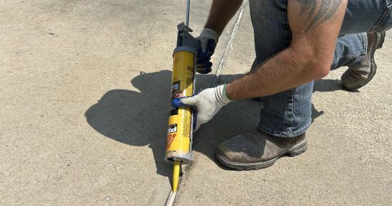 A man is applying a sealant to a concrete surface.