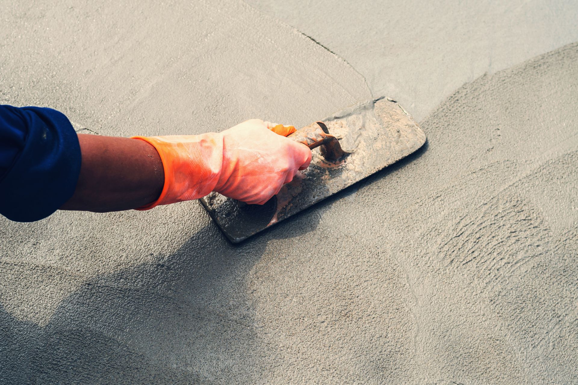 A person wearing orange gloves is using a trowel on a concrete surface.
