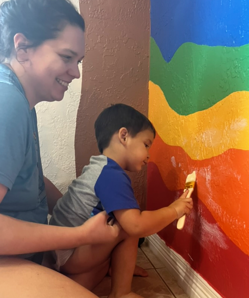 A child is standing in front of a wall with a narwhal painting on it.