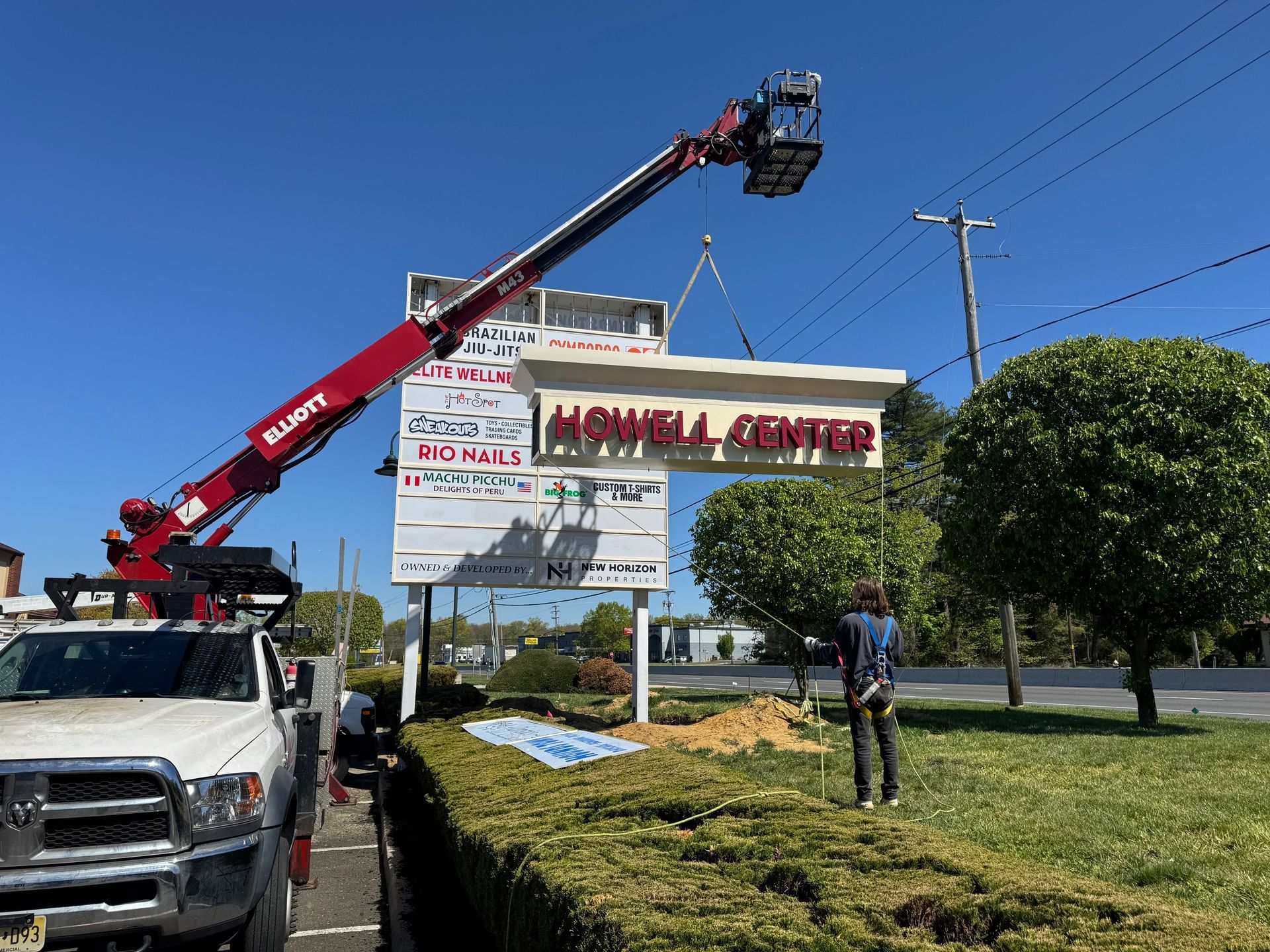 Red crane truck lifting a large sign beside a roadside lawn under a blue sky