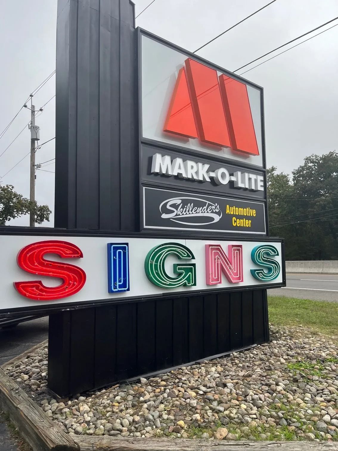 Outdoor business signs: red, white, and green letters on a roadside monument sign under cloudy skies