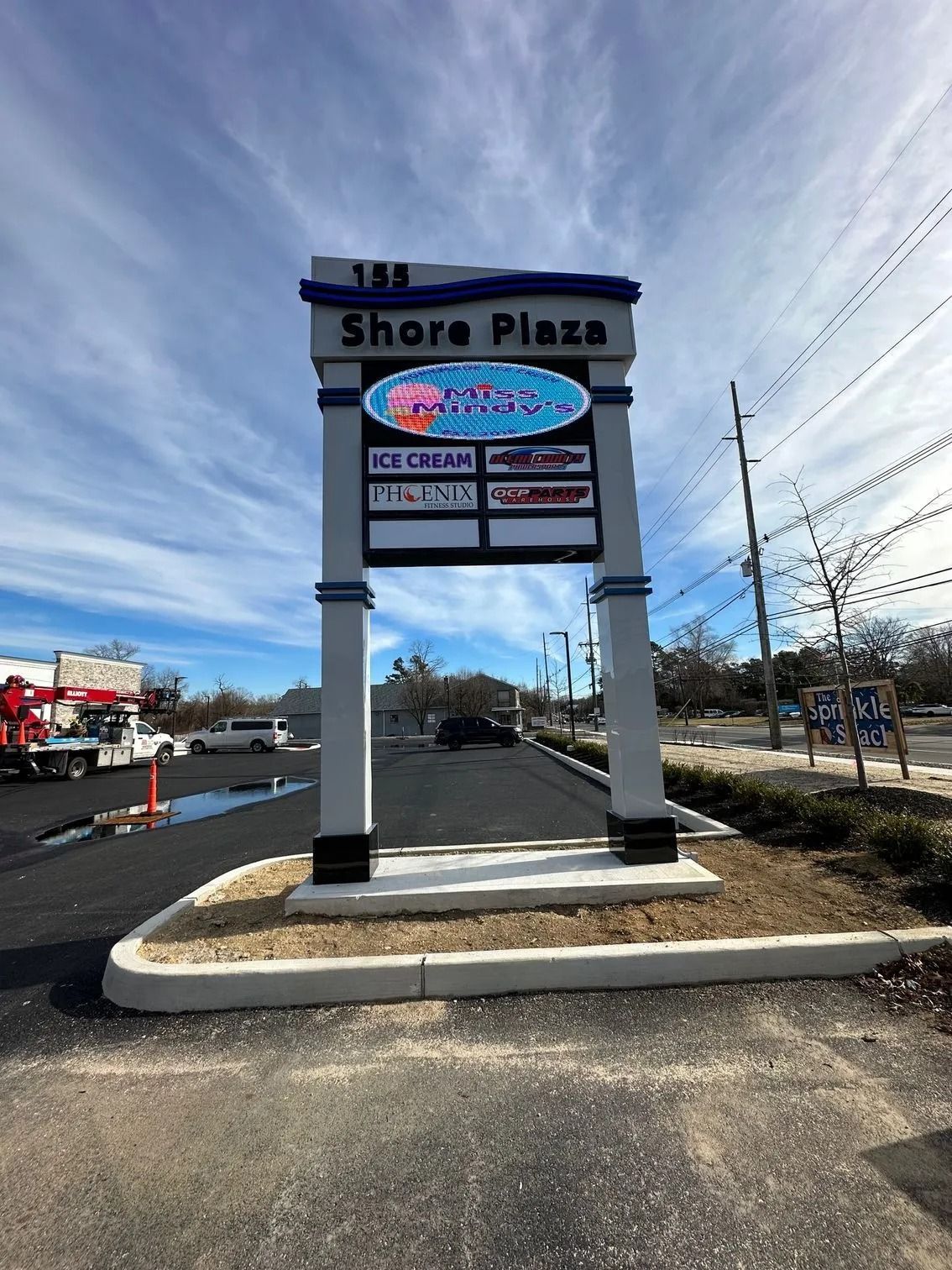 Shore Plaza shopping center sign beside a roadside parking lot on a sunny day