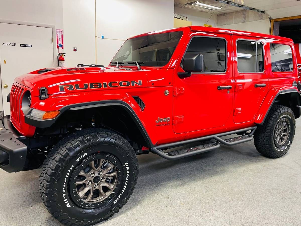 A red jeep wrangler rubicon is parked in a garage.