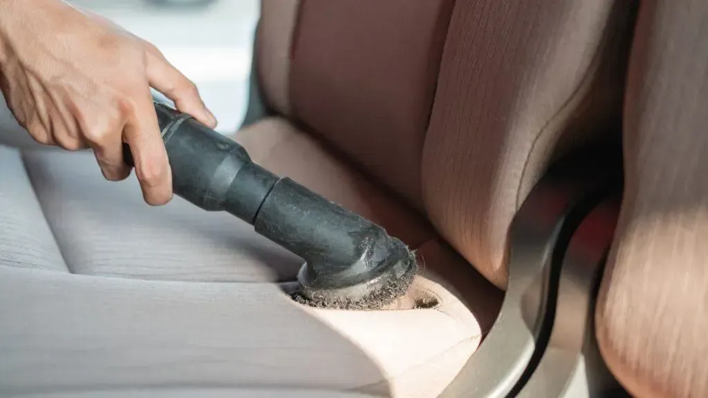 A person is cleaning a car seat with a vacuum cleaner.