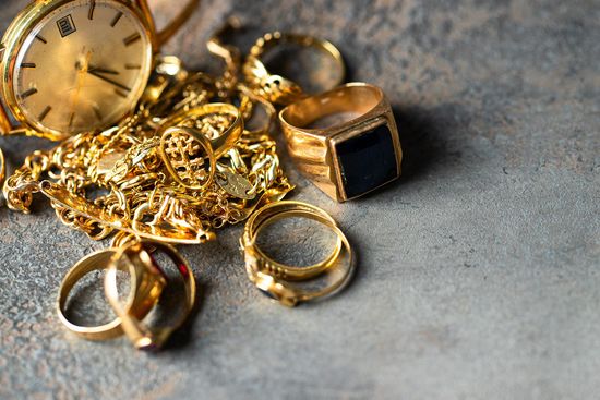 Gold jewelry and a wristwatch scattered on a gray surface