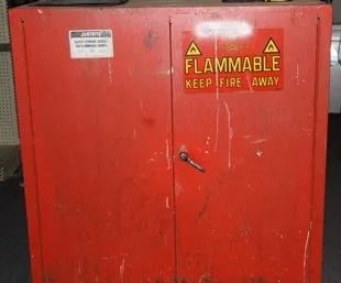 Red metal cabinet with a yellow flammable warning sign and handle lock.