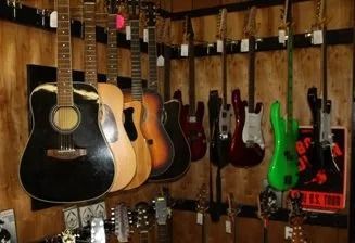 Assorted acoustic and electric guitars hanging on a wall in a music shop or studio.