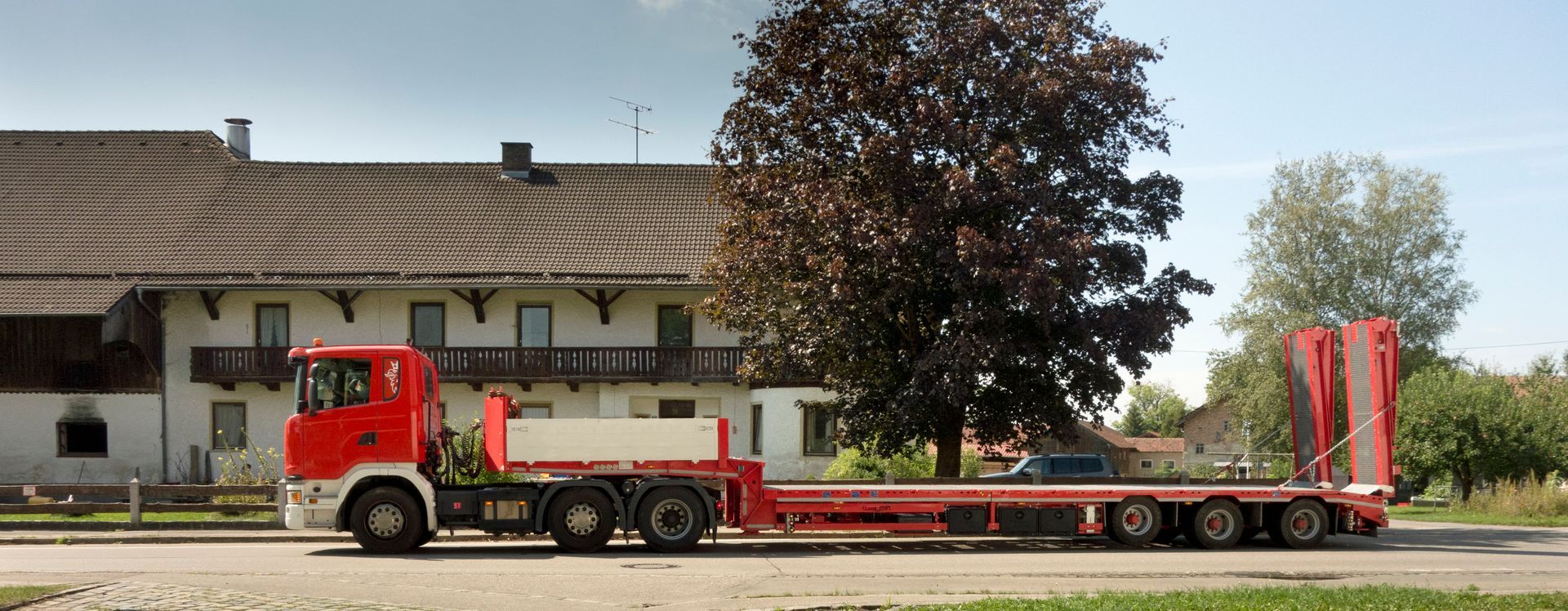 Red flatbed trailer used for heavy duty towing services parked near a countryside home.