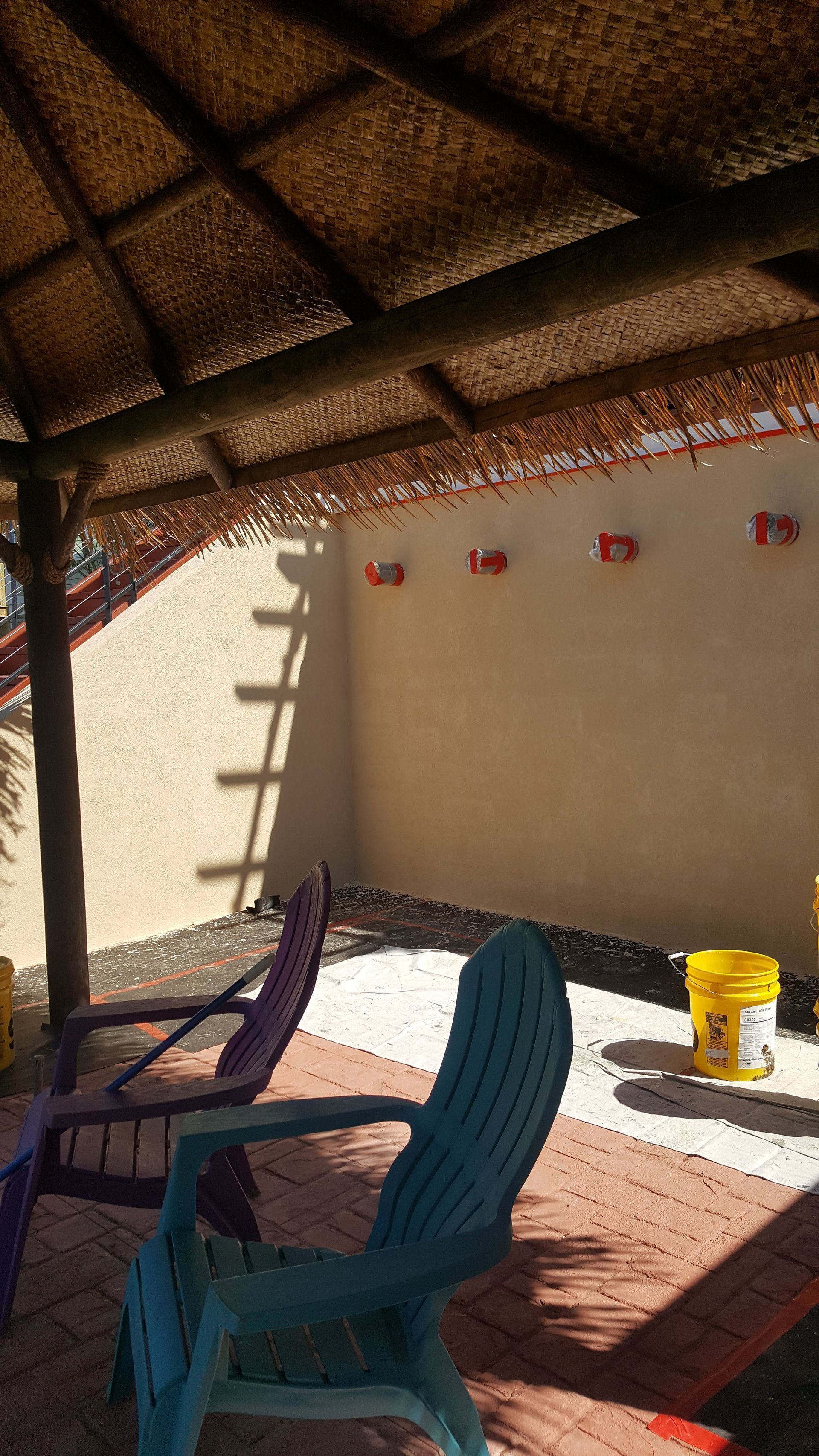 A blue chair is sitting under a thatched roof next to a purple chair.