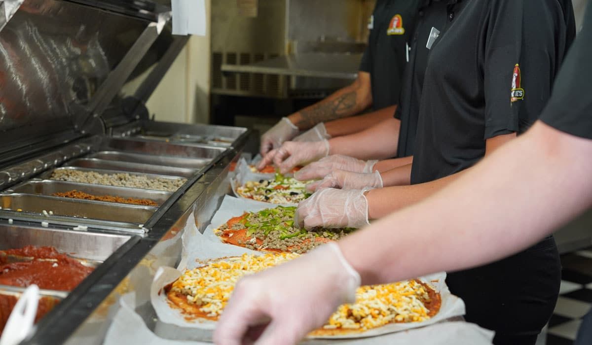 A group of people are preparing pizzas in a kitchen.