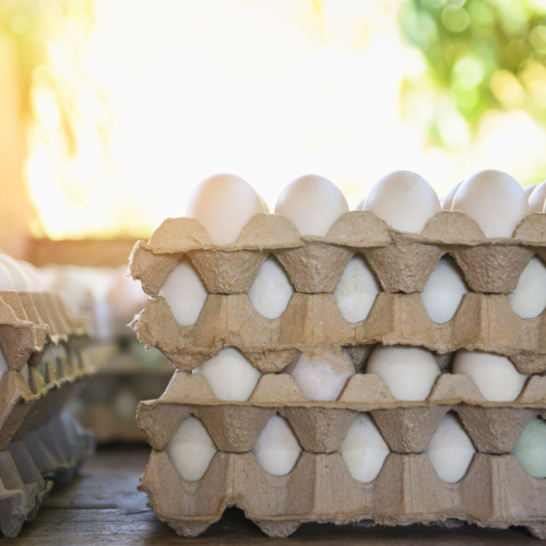 A stack of eggs in cardboard trays on a wooden table.