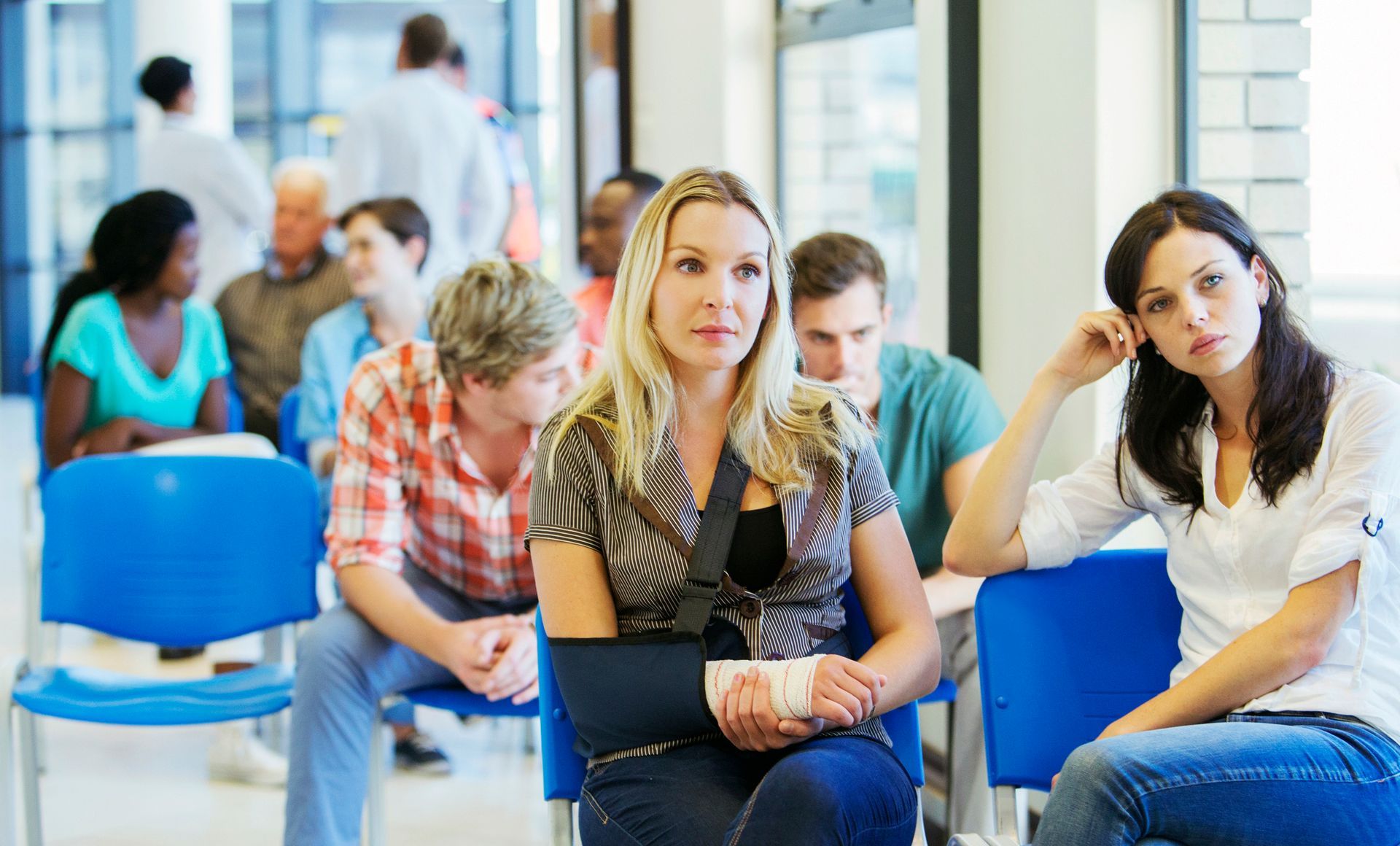 A woman with a cast on her arm is sitting in a waiting room with other people.